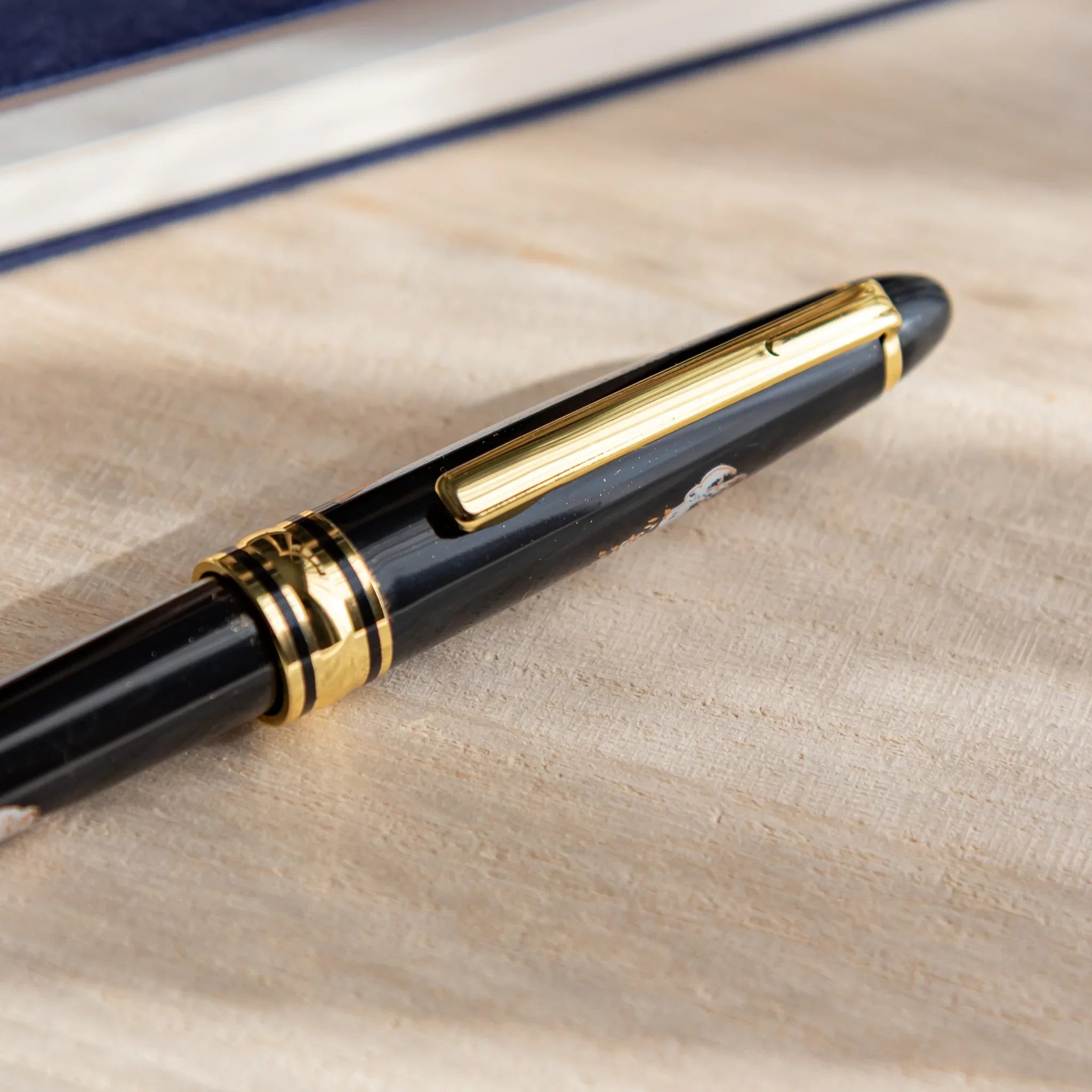 Japanese Ballpoint Pen with Great Wave design placed on a desk, showing black lacquer body, gold clip, and wave artwork detail.