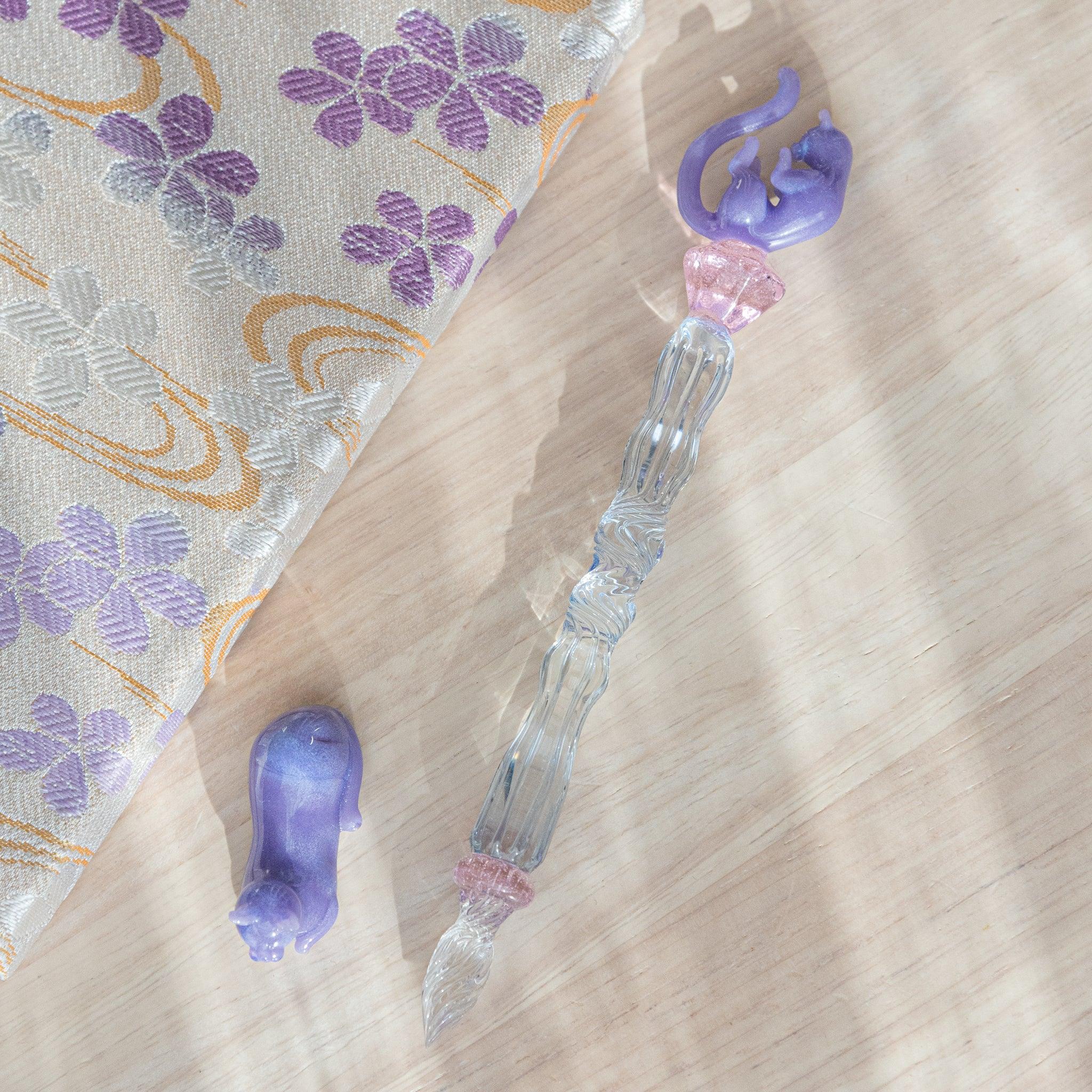 Glass pen with a blue shaft, purple cat design, and pink charm. Includes matching purple pen rest. Perfect for collectors.