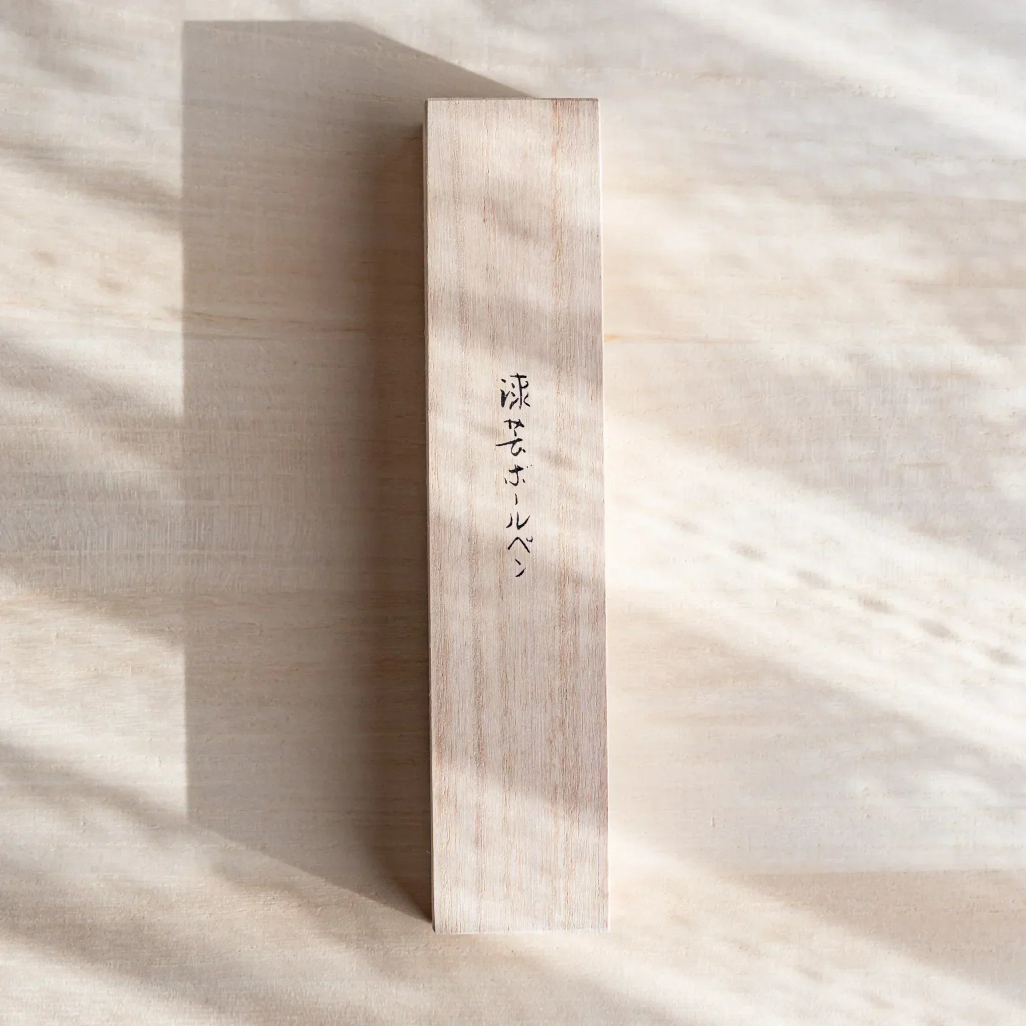 Vertical wooden box with Japanese script designed for a Japanese Ballpoint Pen, shown on a light wood surface.