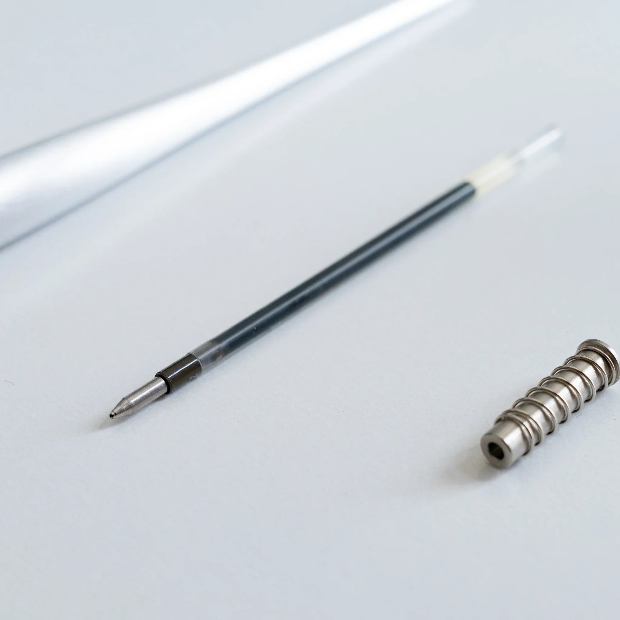 Disassembled ballpoint pen refill with black plastic housing and metal spring coil positioned beside barrel