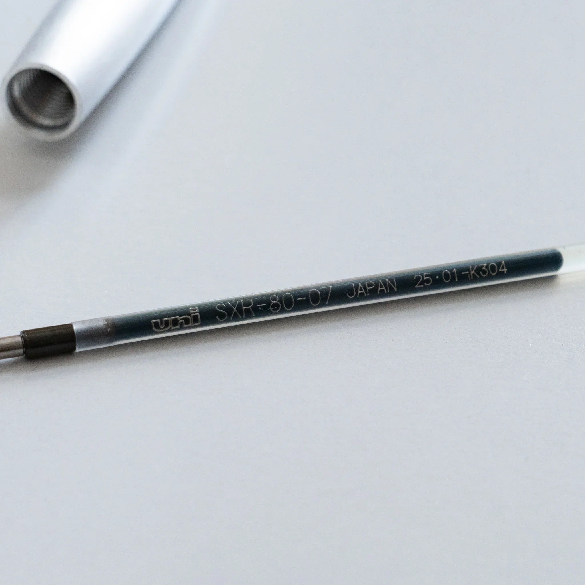 Black ballpoint refill cartridge with visible SHAFT label and SXR-80-07 JAPAN manufacturing code etched deeply