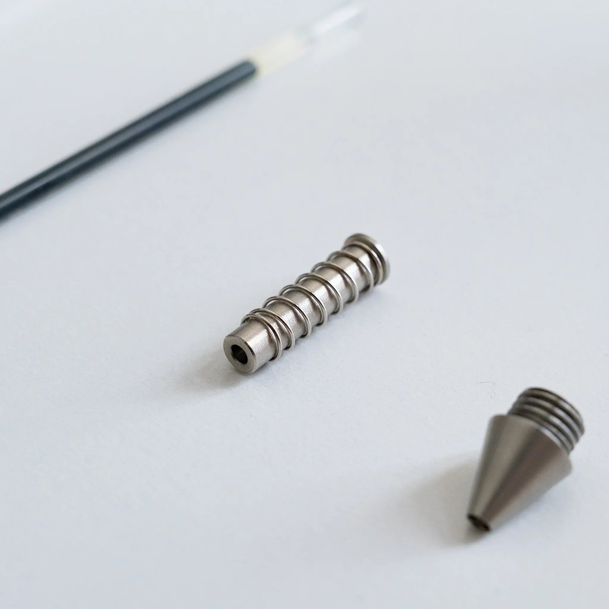 Close-up macro view of spring coil and conical metal ballpoint nib tip components arranged on white surface