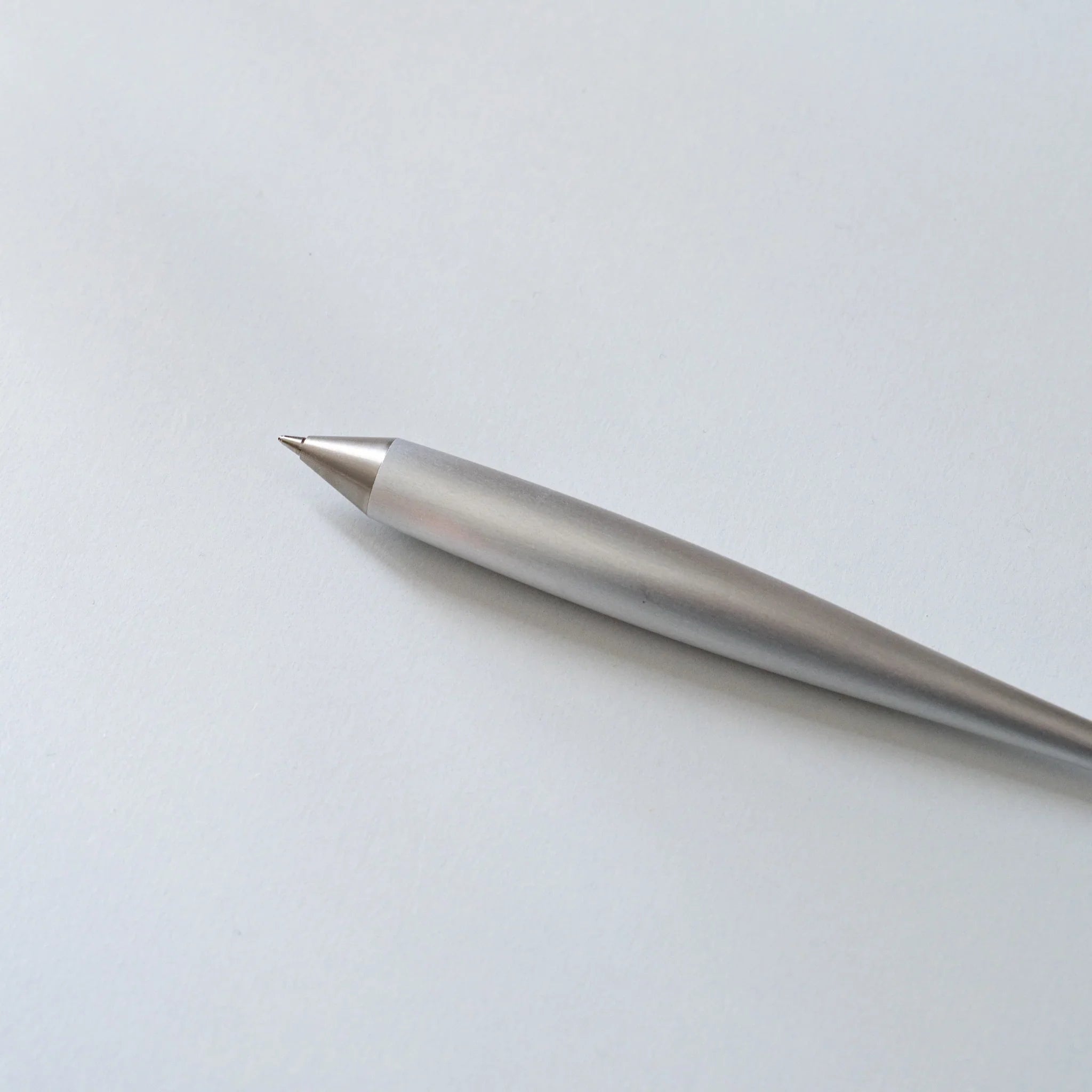 Polished aluminum ballpoint pen angled diagonally on white background showing fine sharp conical tip