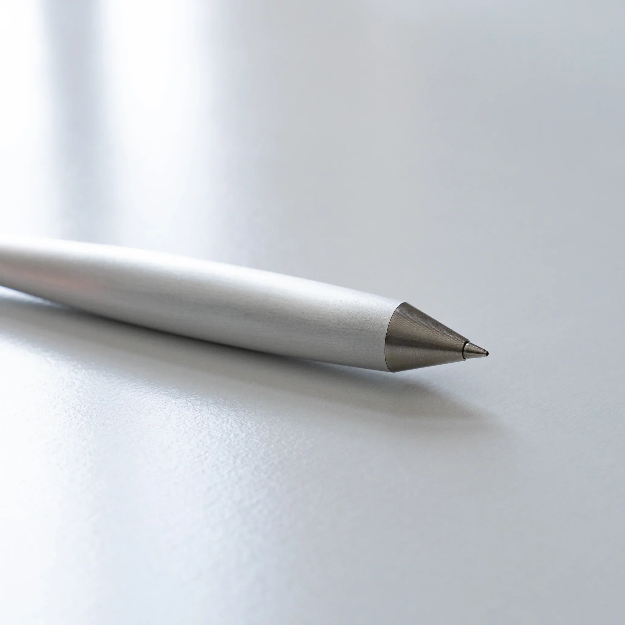 Three-quarter angled view of sleek brushed metal ballpoint pen with prominent cone-shaped sharp tip end