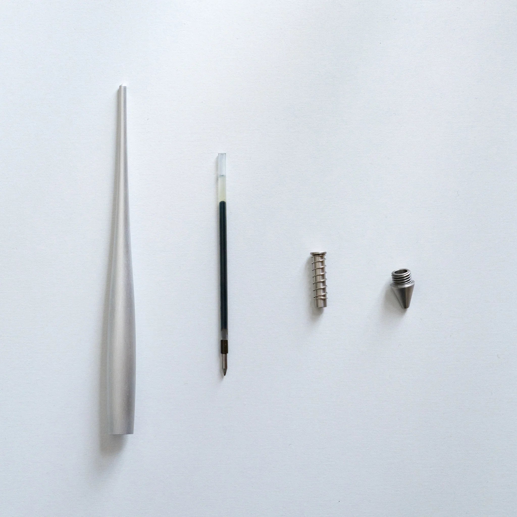 Disassembled ballpoint pen components showing silver aluminum barrel, black refill, metal spring coil, and tip