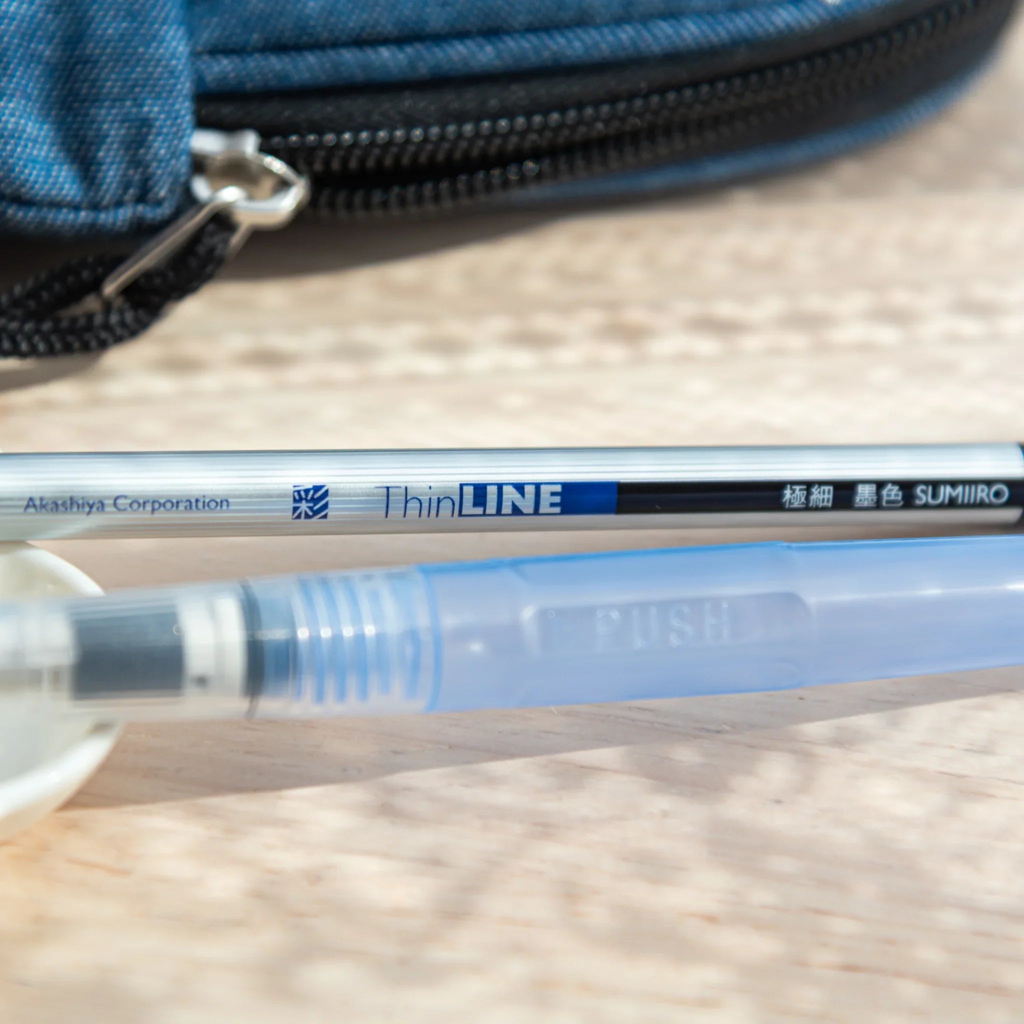 Close-up of Akashiya ThinLINE sumi ink pen next to a water brush, used in arts and crafts painting tools.