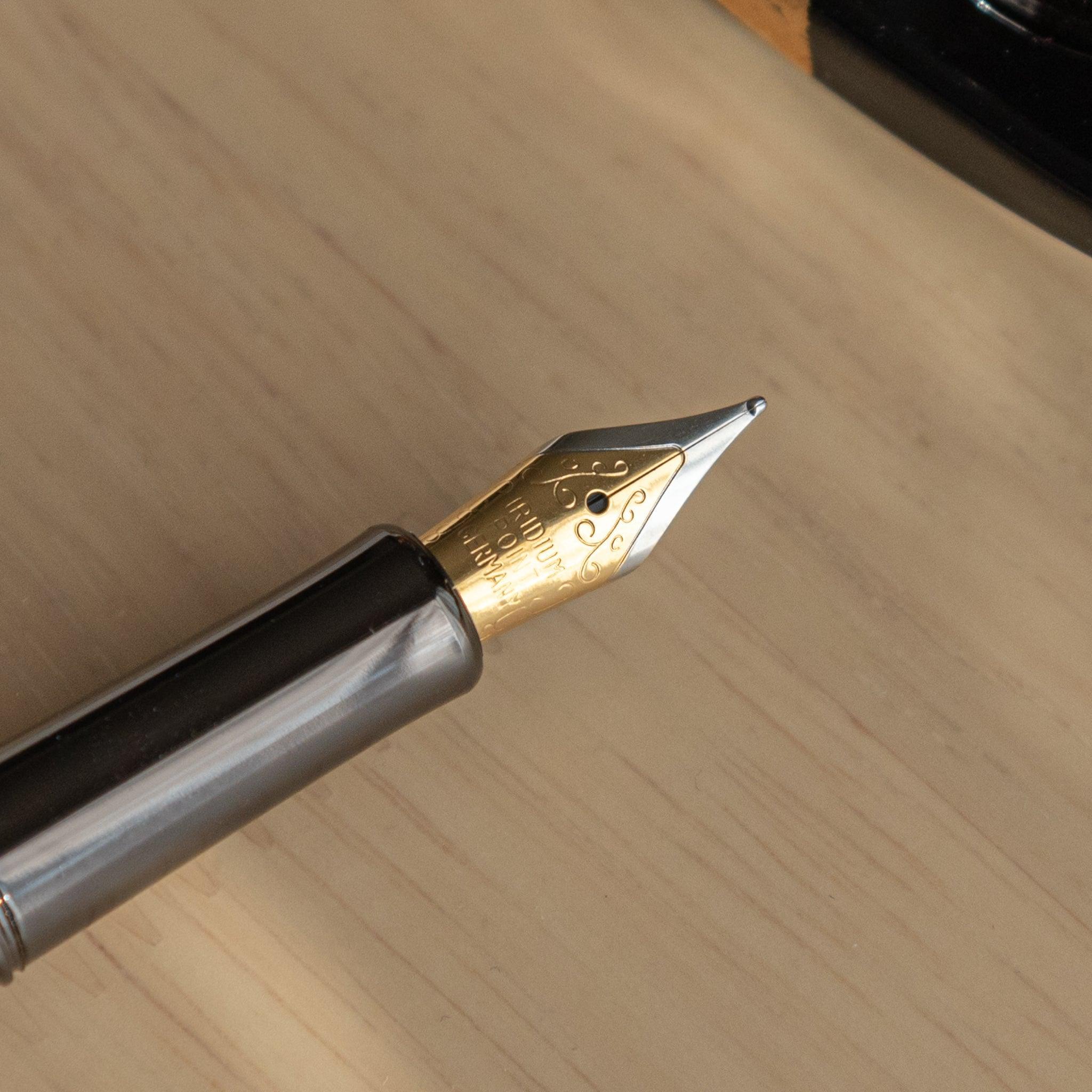 Close-up of a gold fountain pen nib with engraved details, resting on a light wooden desk, showcasing fine craftsmanship.