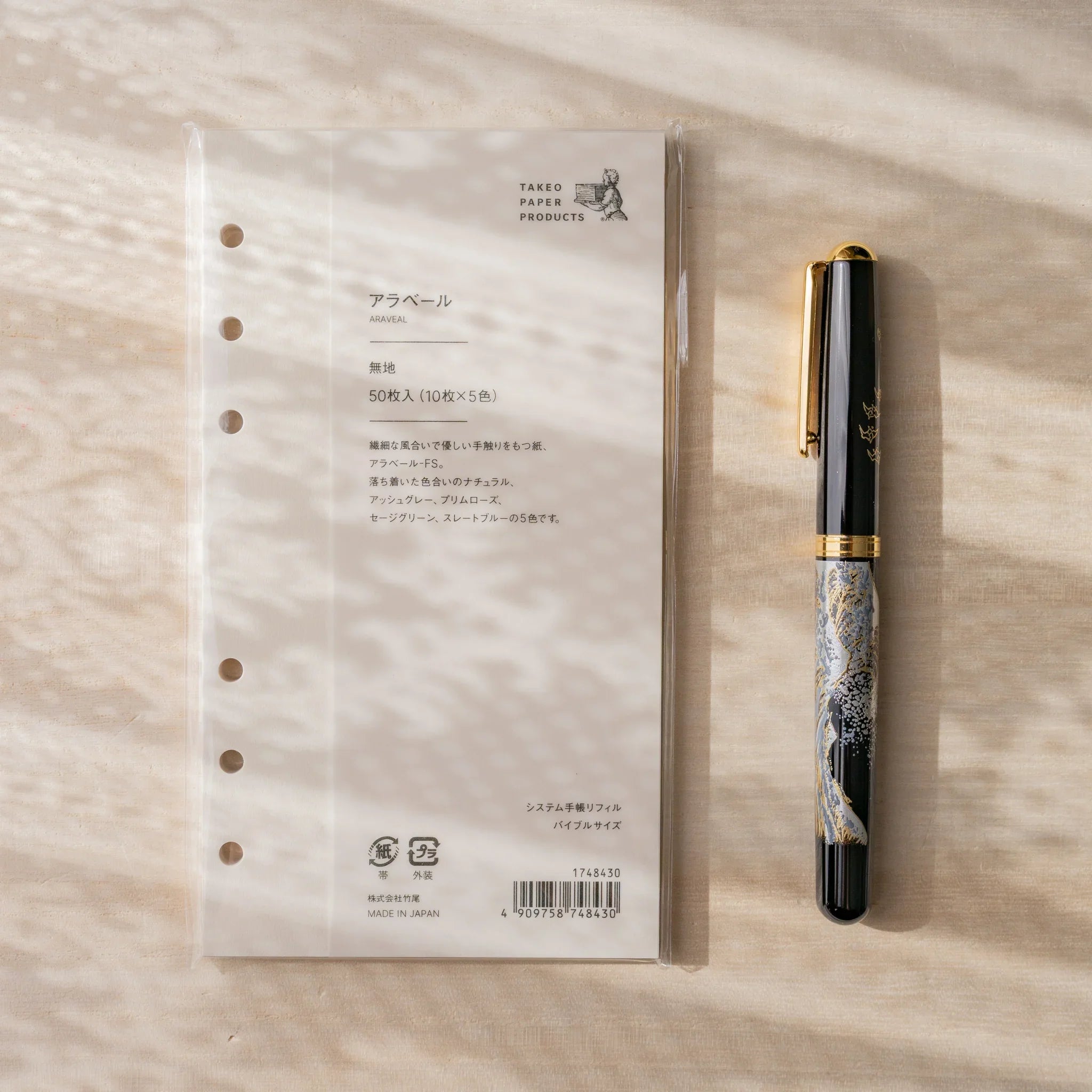 Takeo Paper Araveal Bible-size planner refill packaging with a Japanese fountain pen alongside on a wood surface.
