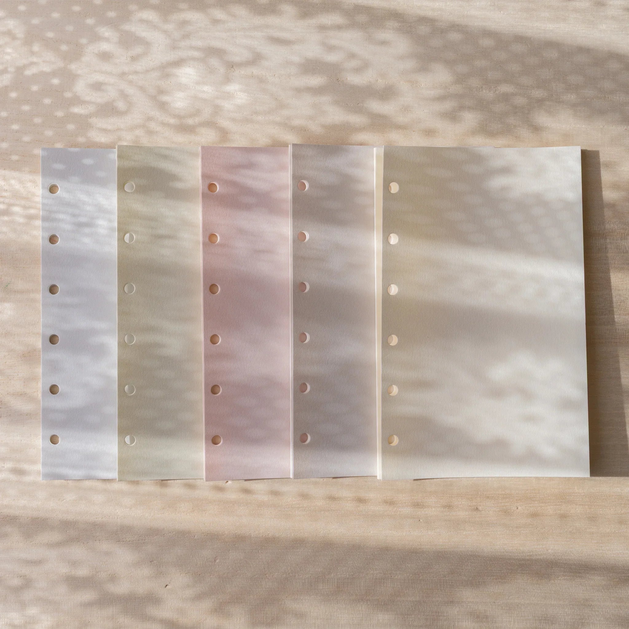 Five Araveal Mini 6 planner refill papers laid flat side by side showing 6-hole binder punch.