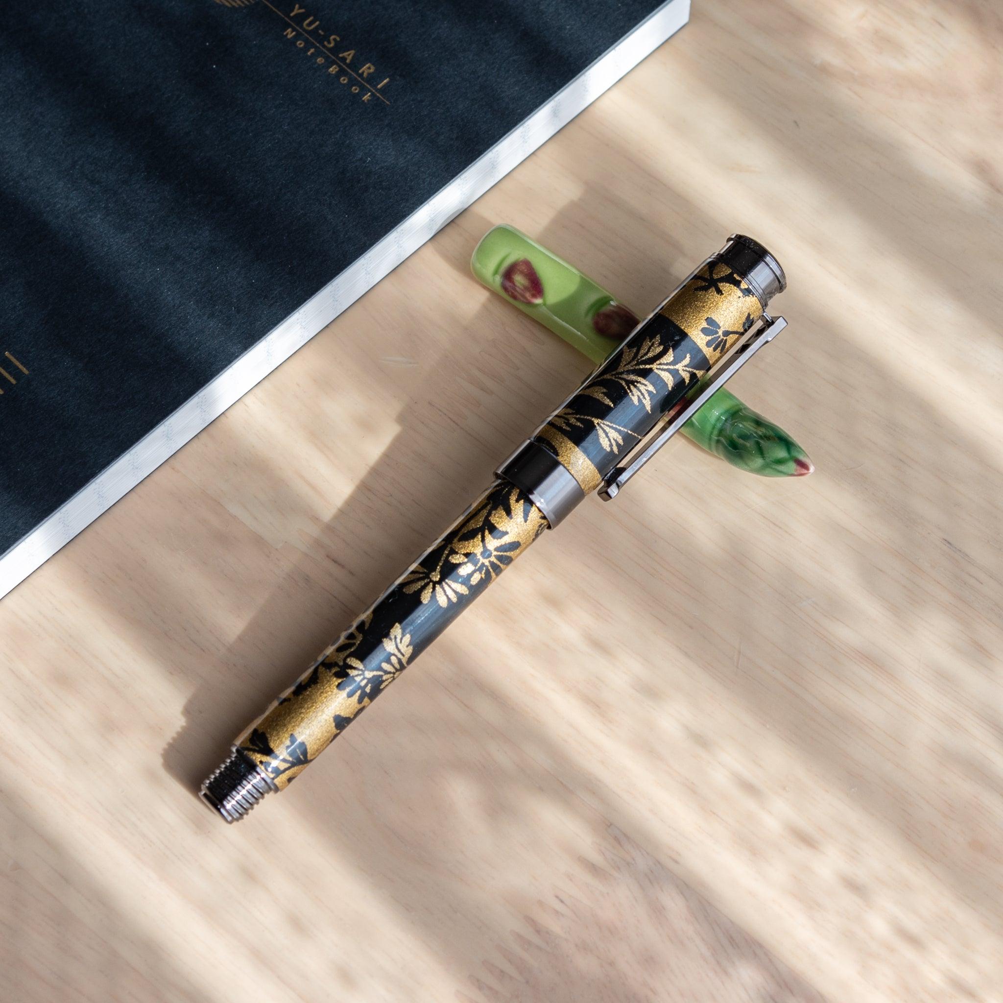 A handmade green ceramic pen rest shaped as an asparagus, holding a black and gold fountain pen. Part of traditional Japanese stationery items.