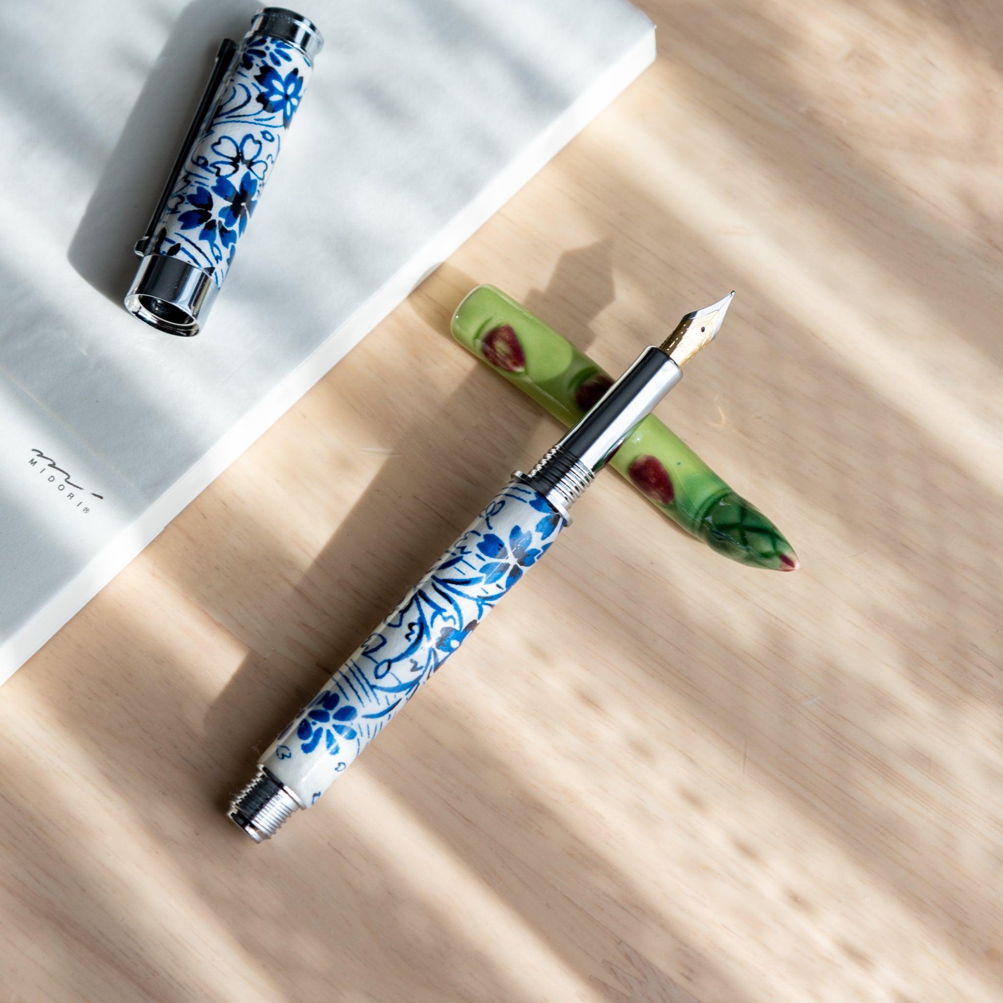 A handmade green ceramic pen rest shaped as an asparagus, holding a blue and white porcelain fountain pen. Part of Japanese stationery items.