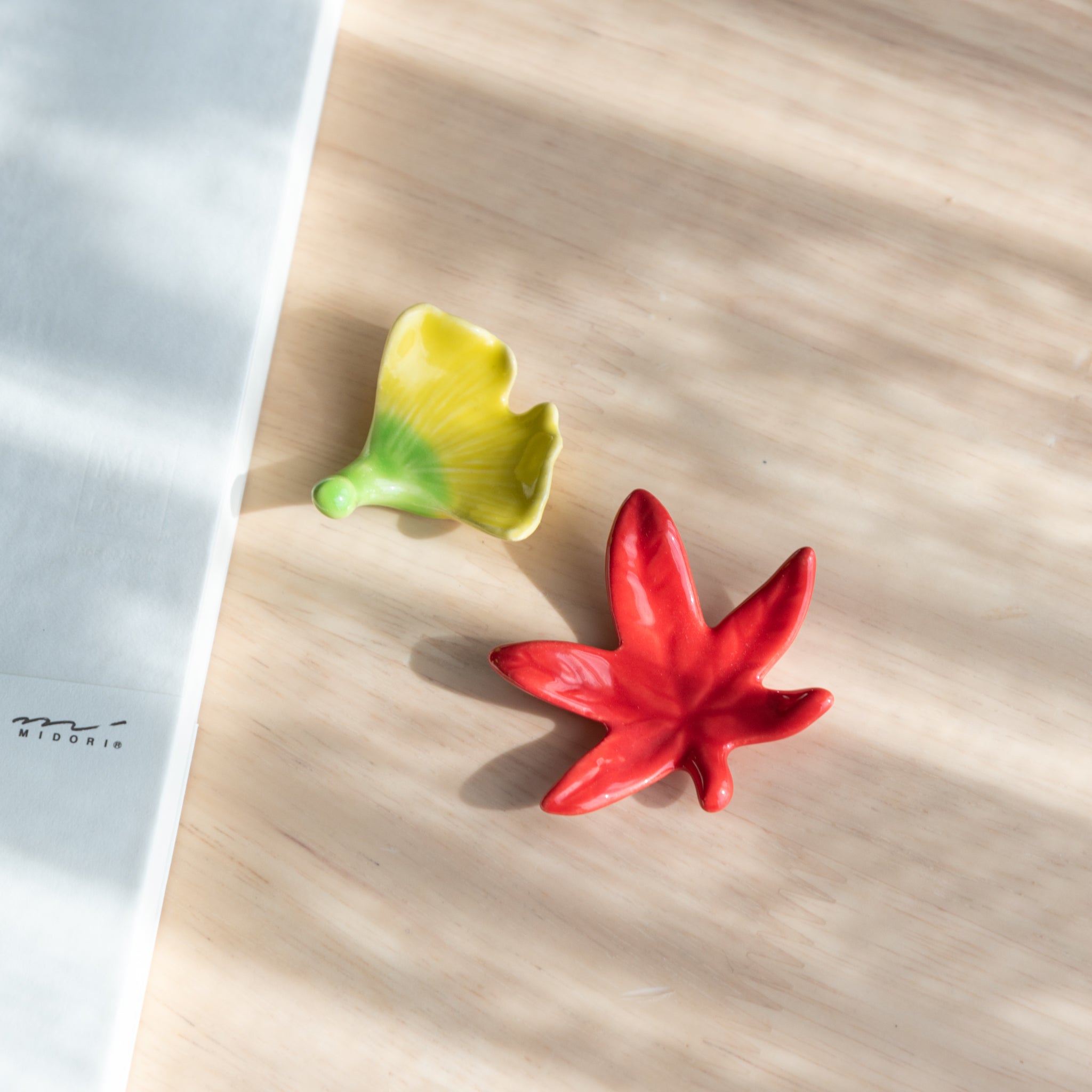 Handmade ceramic pen rests shaped as a red maple leaf and a yellow ginkgo leaf, part of traditional Japanese stationery with seasonal design.