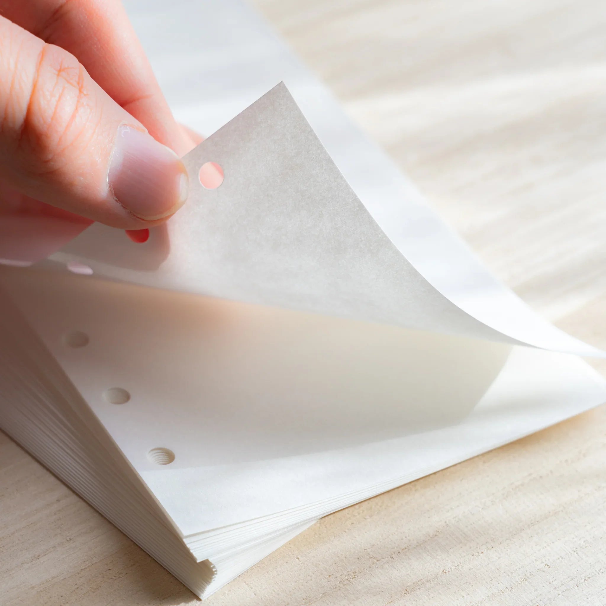 Japanese Stationery bank paper refill sheet being lifted, showing its thin white texture and six-hole punches on a stacked planner pad.