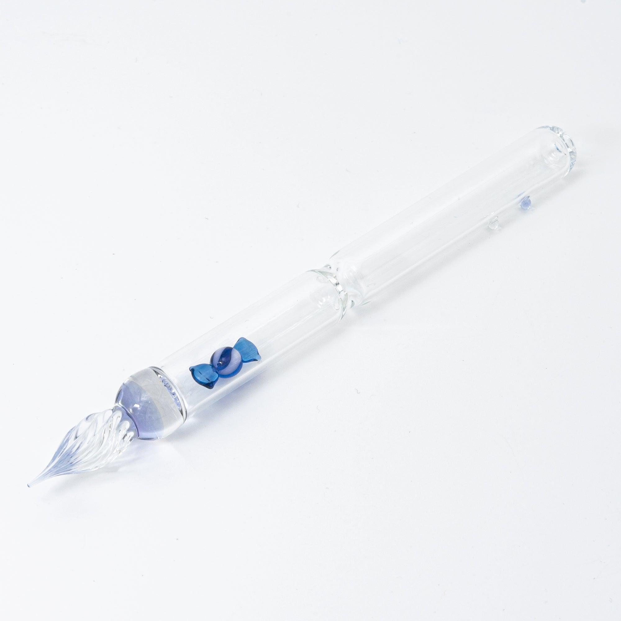 A clear glass dip pen with a small blue candy-shaped glass motif captured inside its shaft. The pen’s nib is intricately designed, enhancing the overall charm.