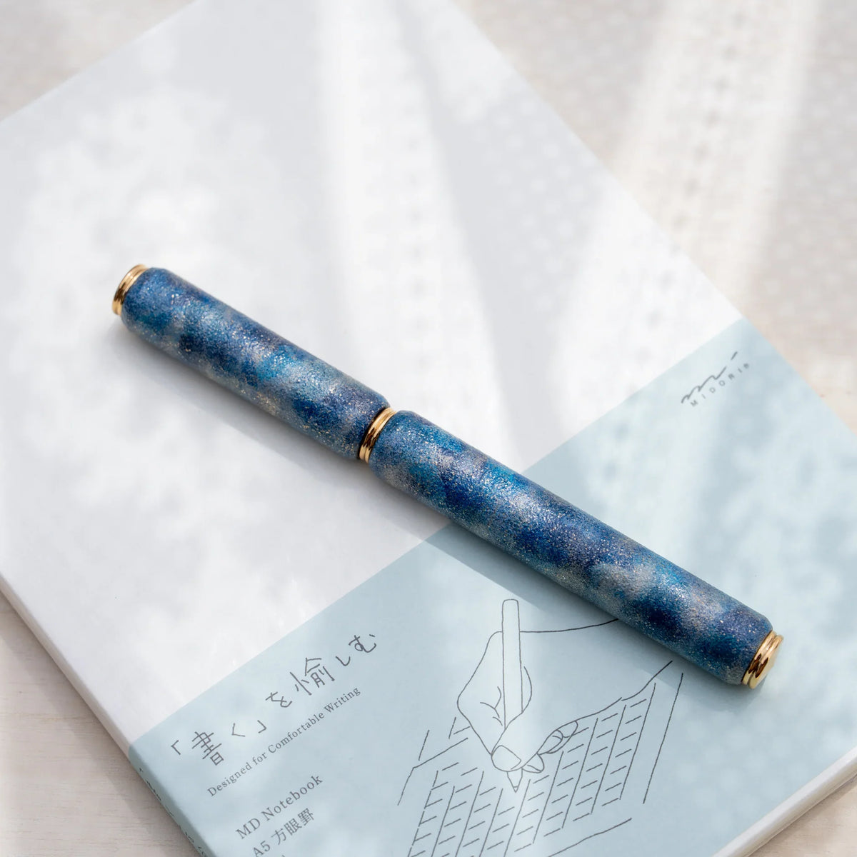 Blue marbled urushi lacquered rollerball pen in zelkova wood, resting on a Japanese notebook