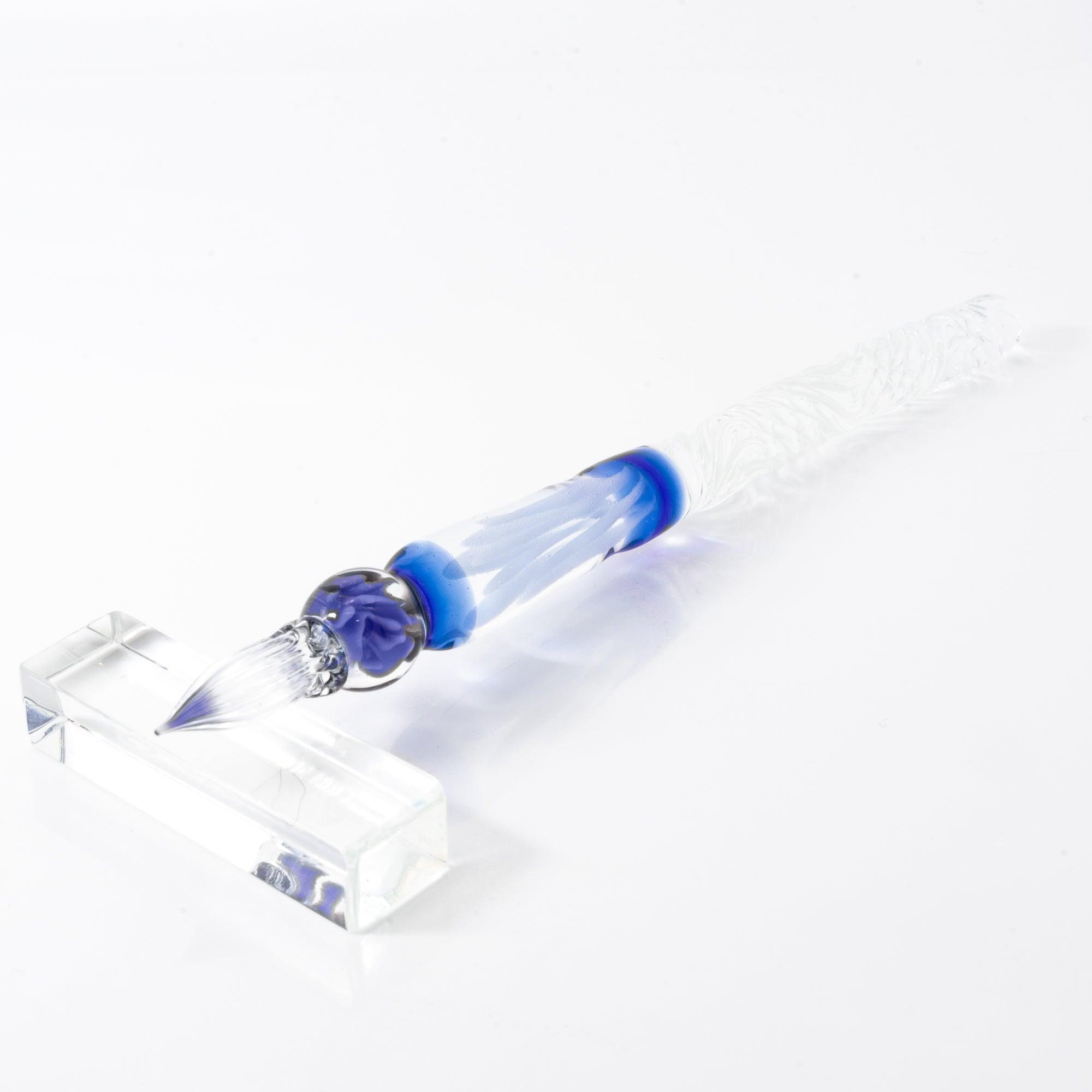 A delicate glass pen with an intricate blue rose motif, resting on a clear pen holder.