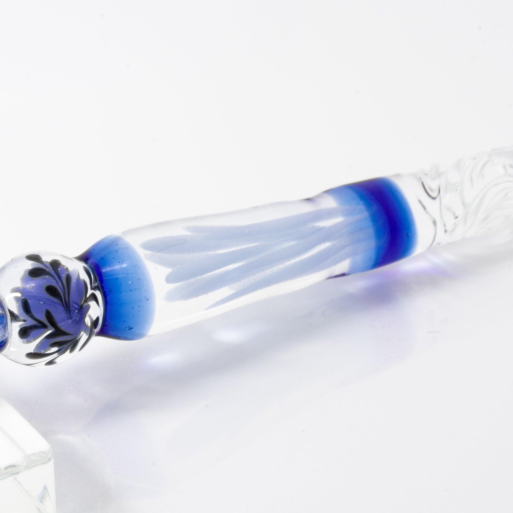 A delicate glass pen with an intricate blue rose motif, resting on a clear pen holder.