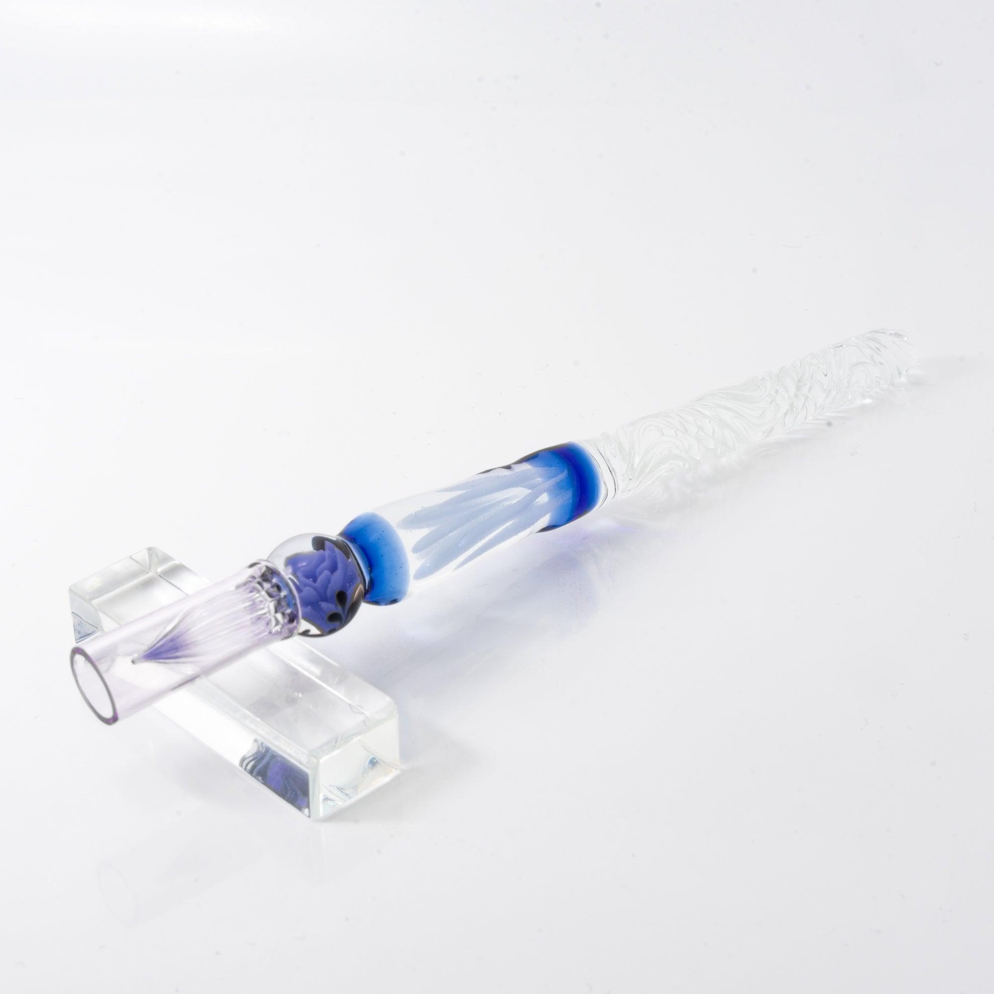 A delicate glass pen with an intricate blue rose motif, resting on a clear pen holder.