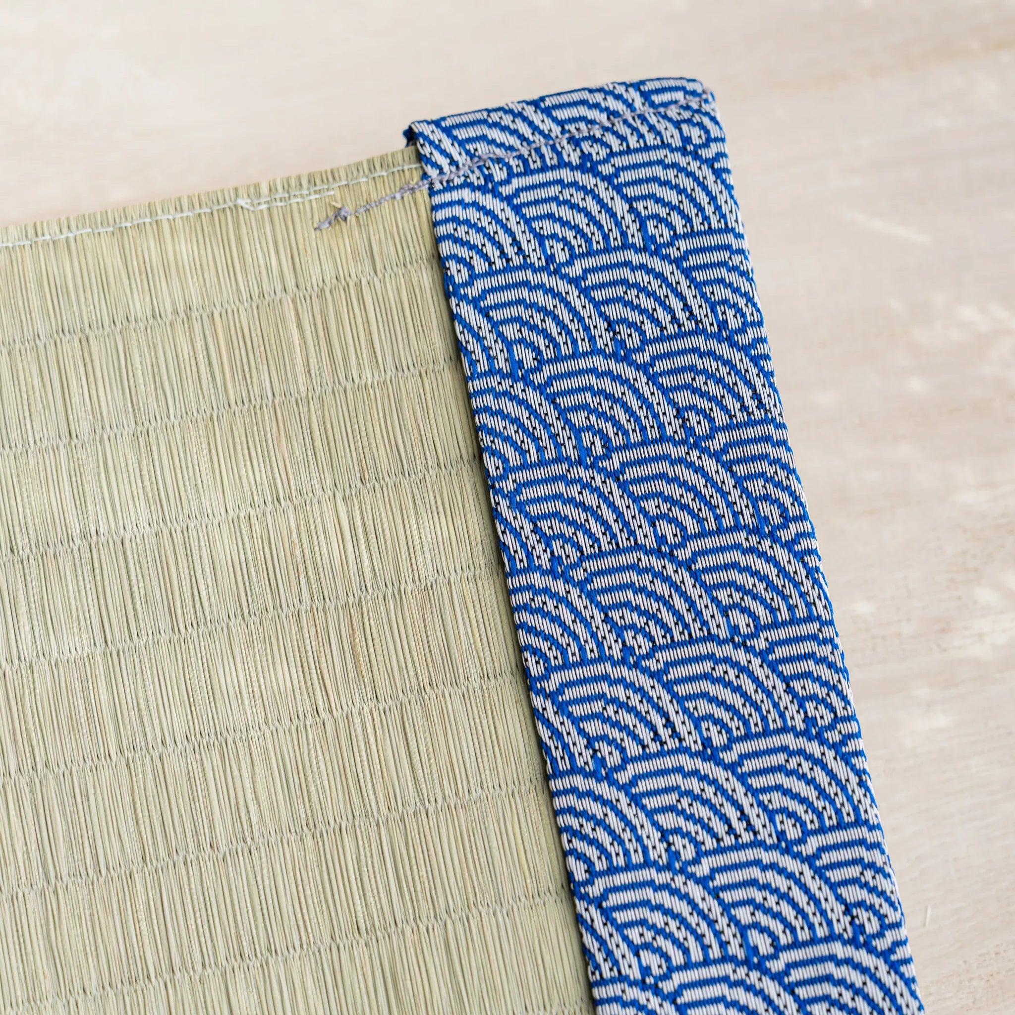 Close-up of blue and white Japanese wave pattern brocade band beside woven green rush straw at the cover corner