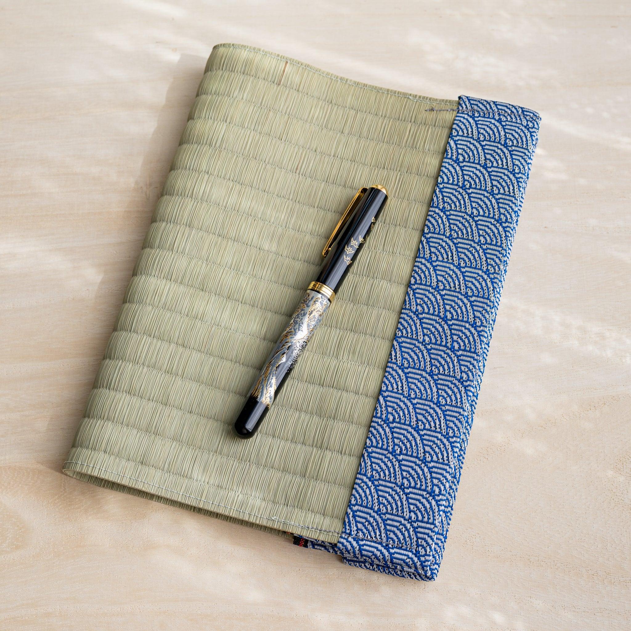 Black and gold fountain pen resting on closed tatami book cover with blue and white wave pattern fabric band
