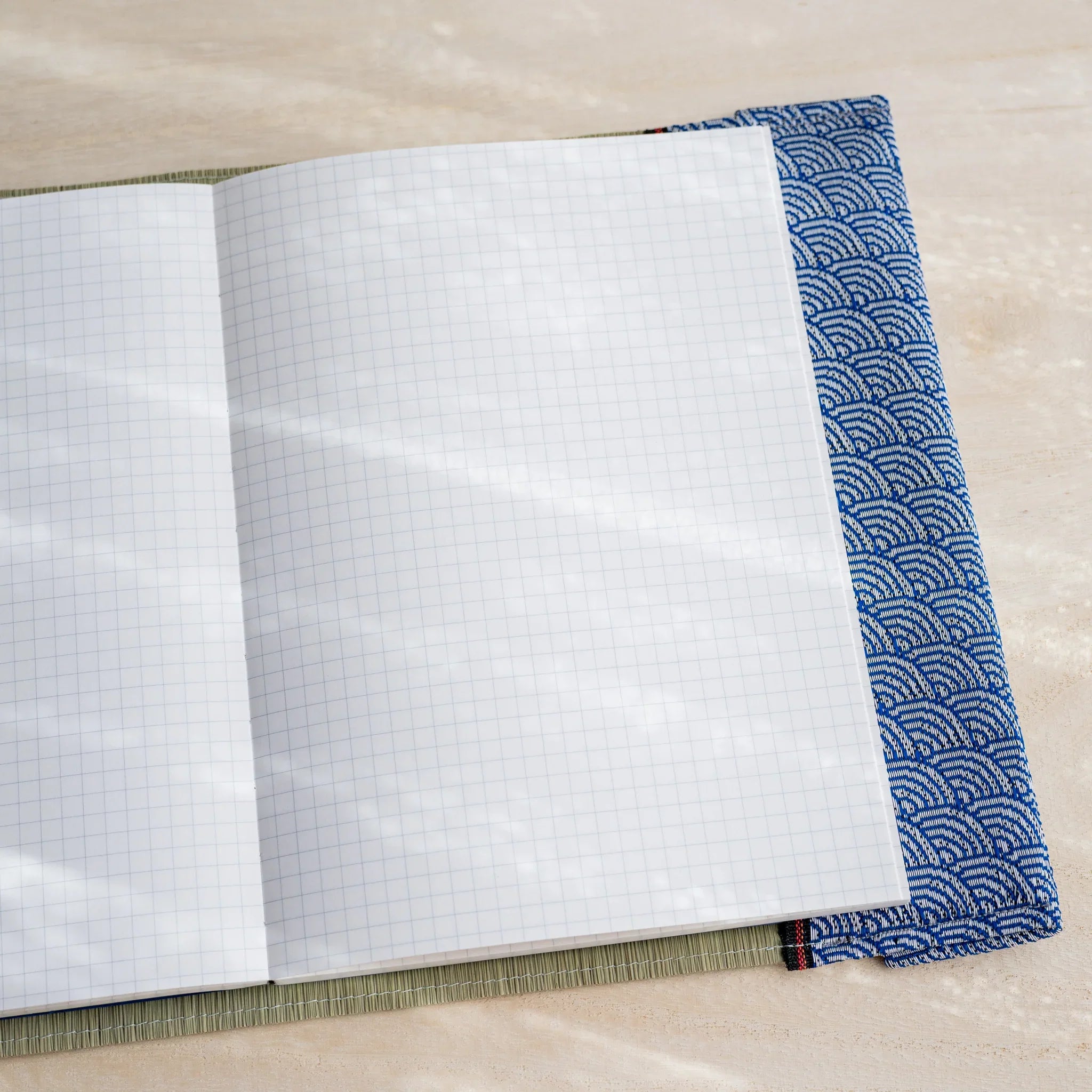 Angled view of tatami book cover open to white grid notebook pages with blue and white wave pattern fabric edge