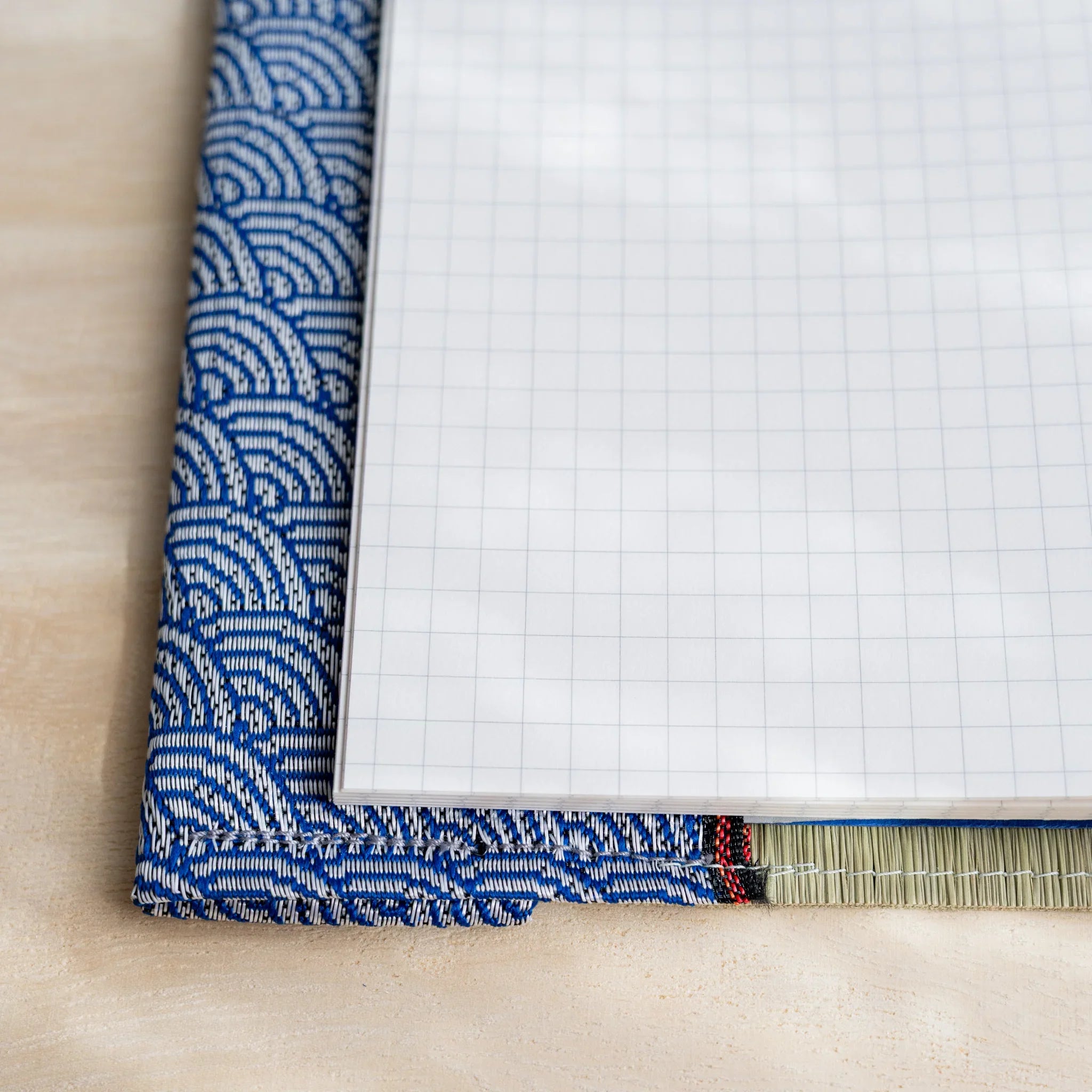 Corner close-up of white grid notebook page inside the tatami cover with blue and white wave pattern fabric flap