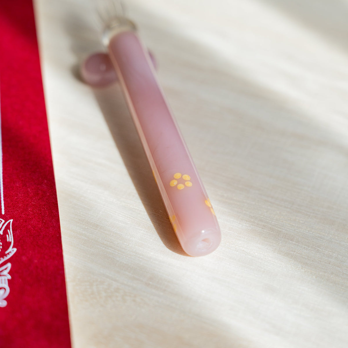 Blush Pink Flowers pen barrel angled across pale wood with yellow blossom motifs and a red card behind