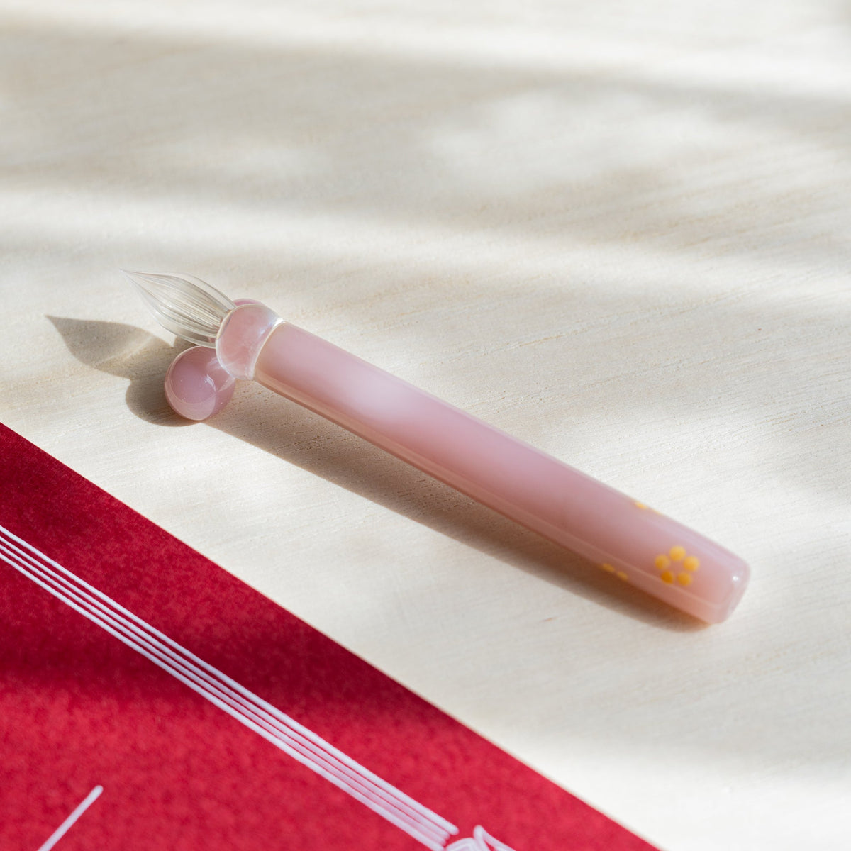Blush Pink Flowers glass dip pen laid on pale wood, pink barrel with a yellow blossom near the end