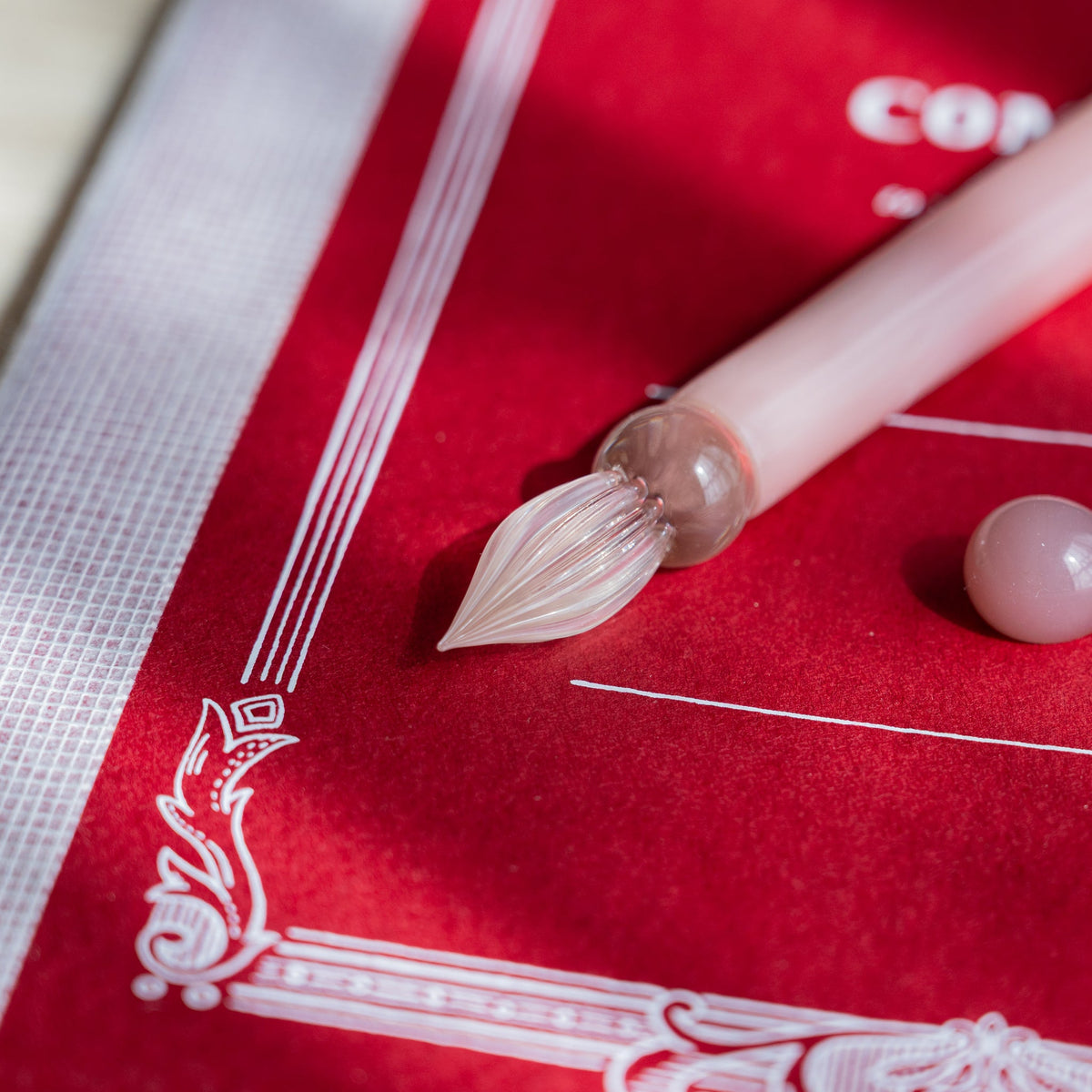 Clear fluted nib of the Blush Pink Flowers glass dip pen with a pale pink glass sphere beside it