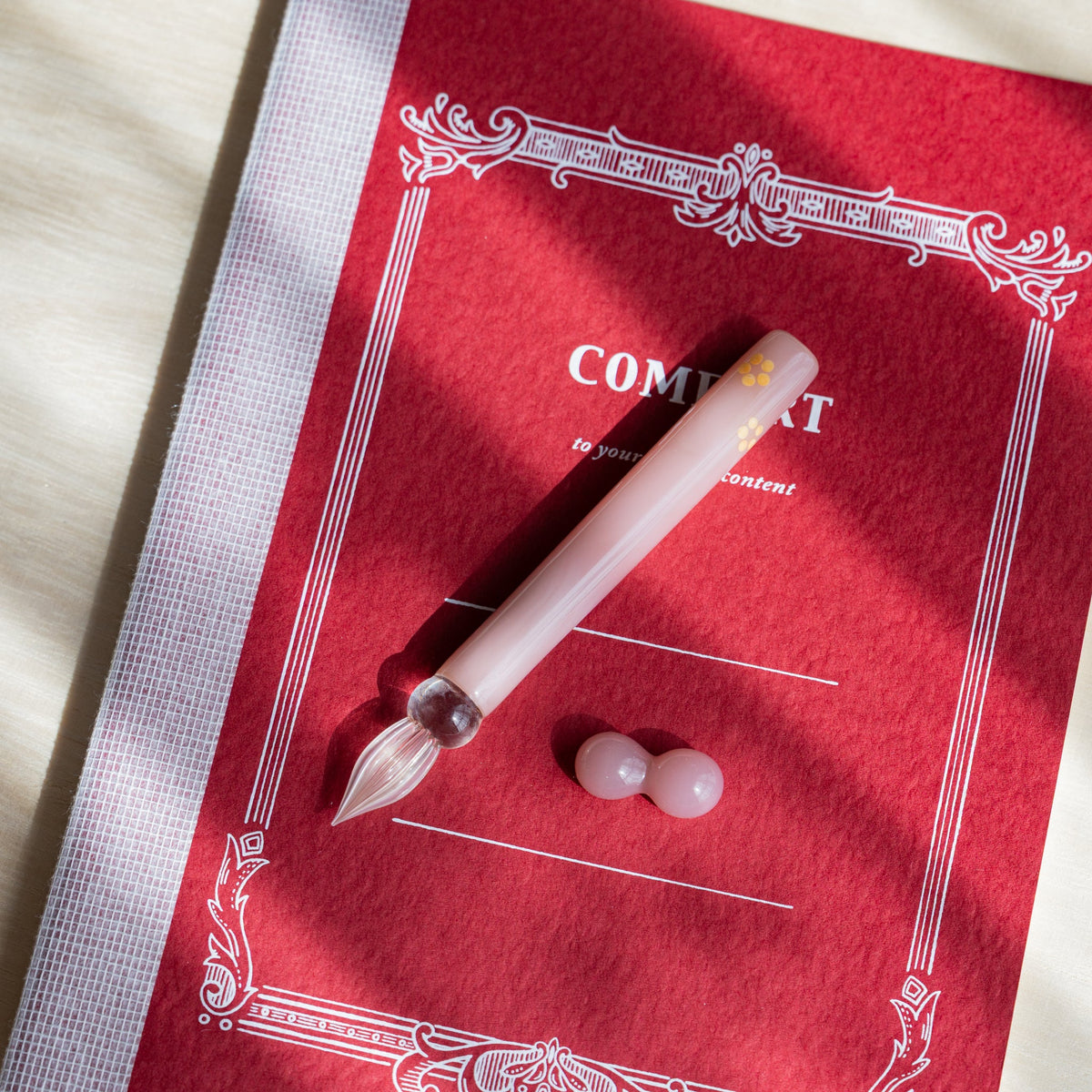 Blush Pink Flowers glass dip pen and its two-sphere pink pen rest on a red card with a white printed frame