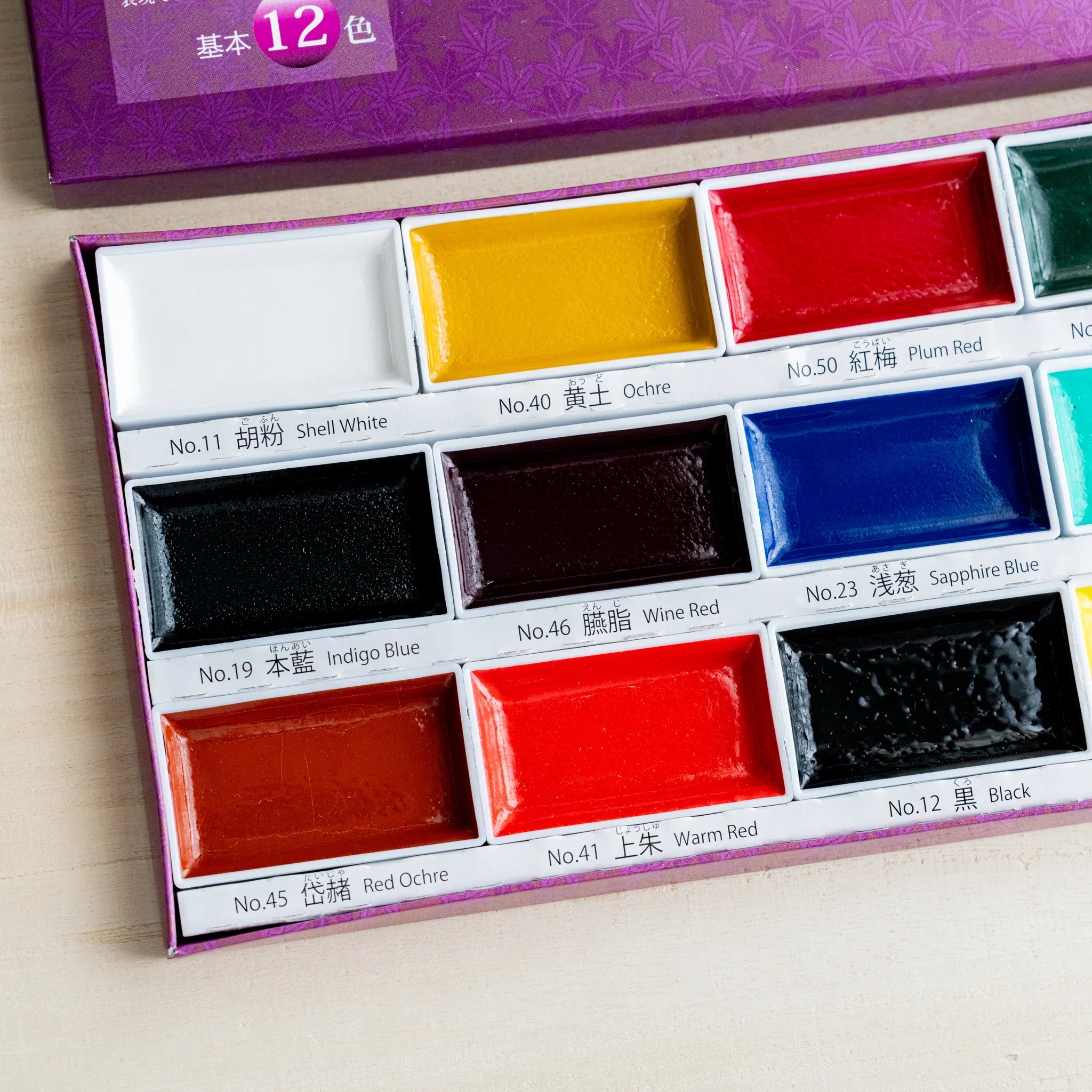 Close-up of Gansai 12-color watercolor box showing nine traditional Japanese color pans with bilingual labels