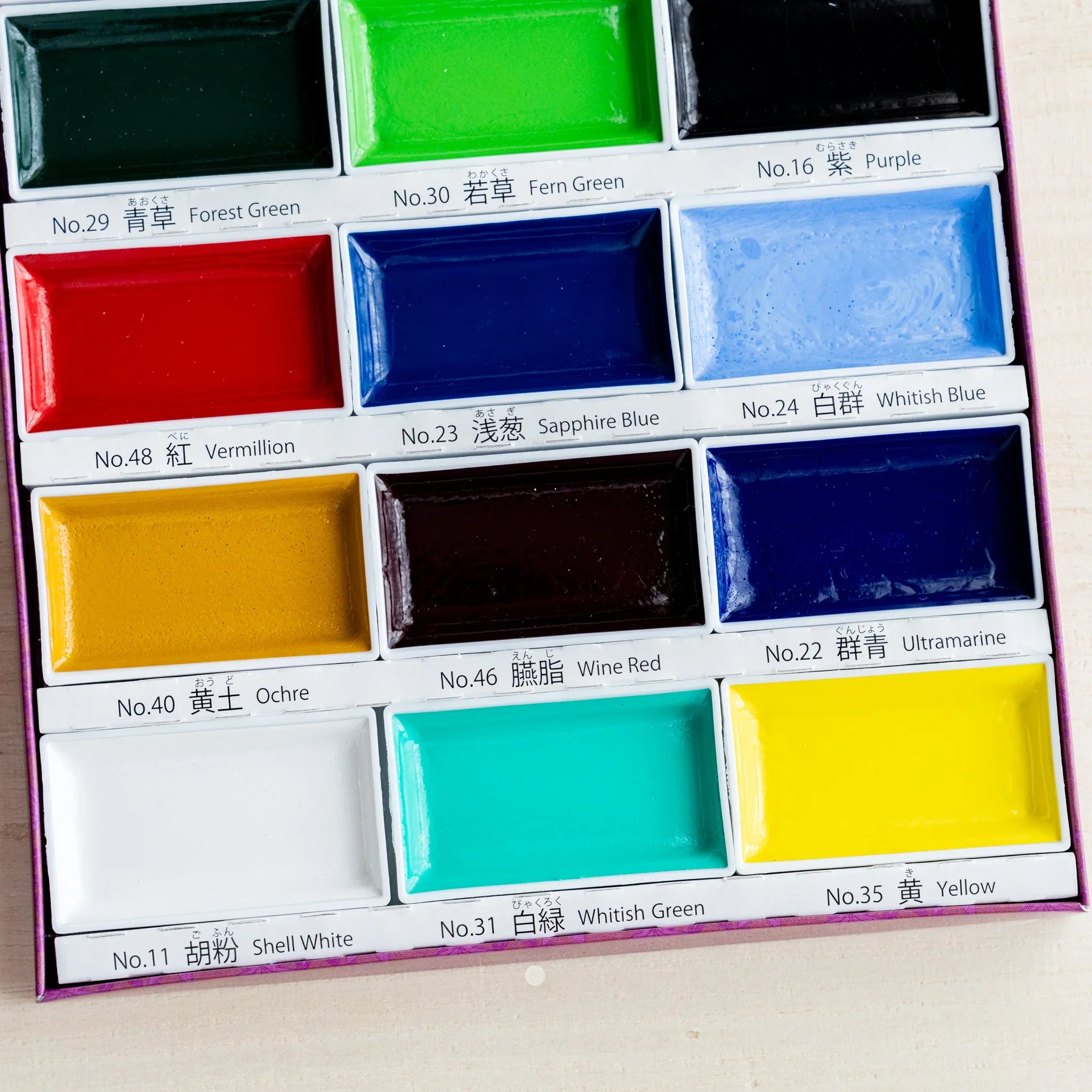 Close-up of lower portion of Gansai 18-color watercolor box showing twelve pans including Shell White and Yellow