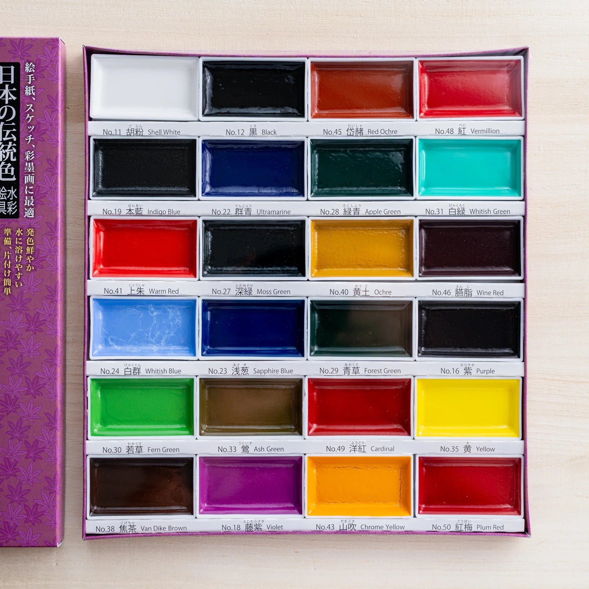 Open Gansai 24-color box from above showing twenty-four dry watercolor pans in six rows of four, with bilingual labels