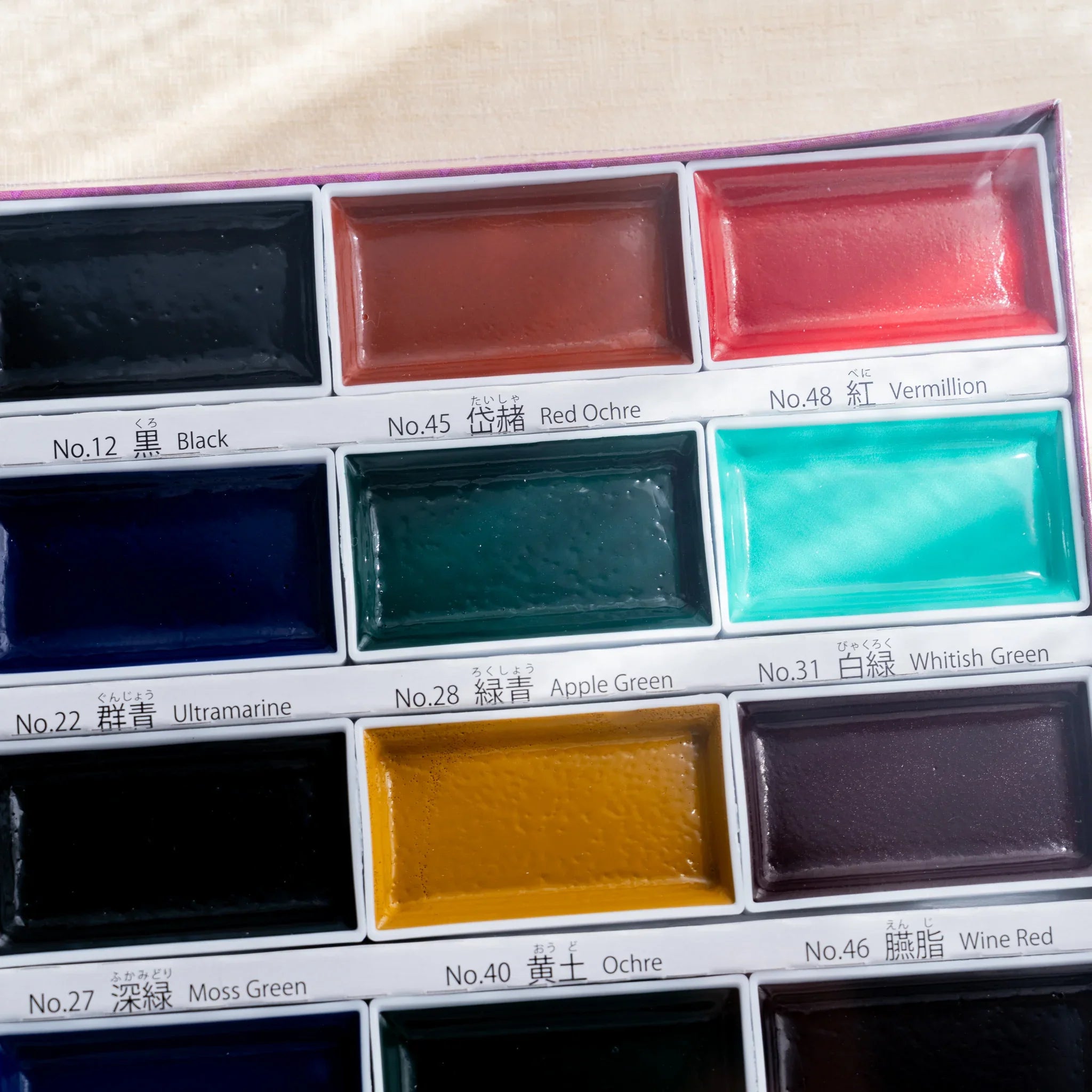 Close-up of upper portion of Boku-Undo Gansai 24-color watercolor box showing twelve pans with traditional color labels