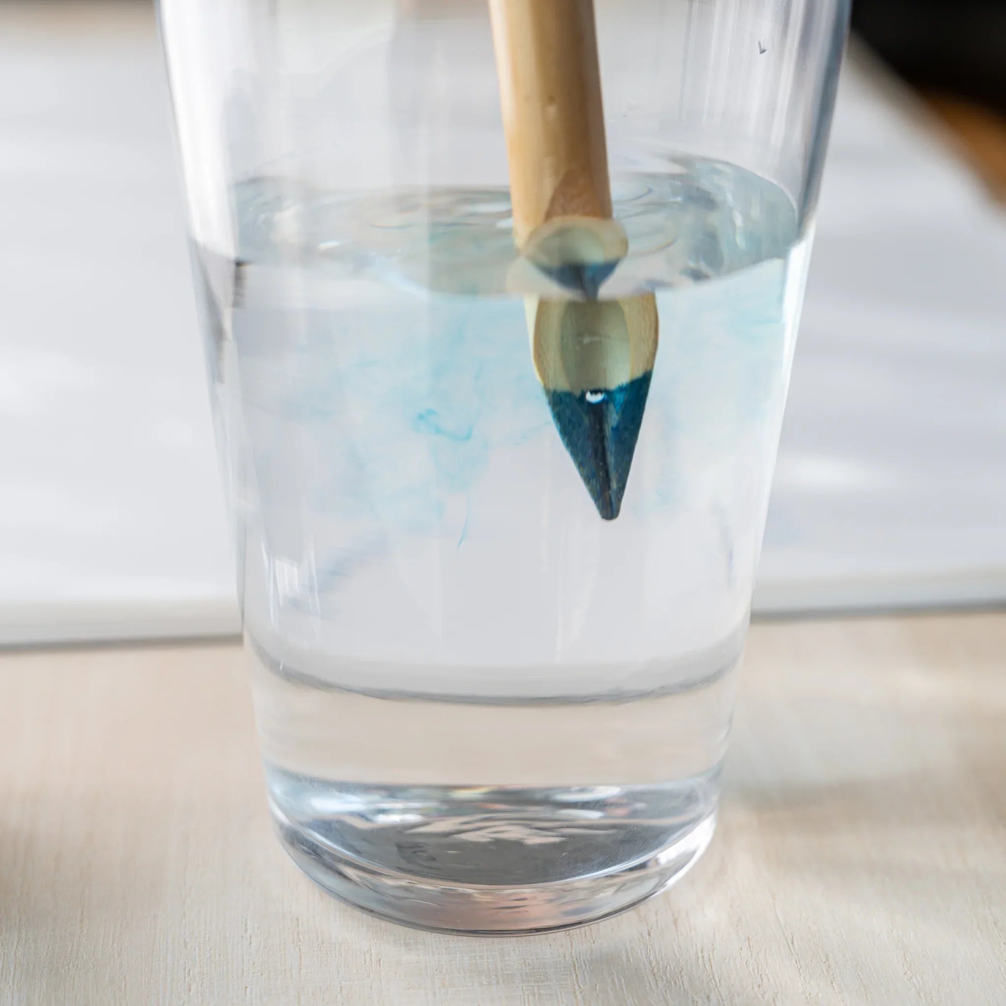 Close-up of Boku-Undo bamboo dip pen nib submerged in water, blue ink diffusing from the tip into the glass