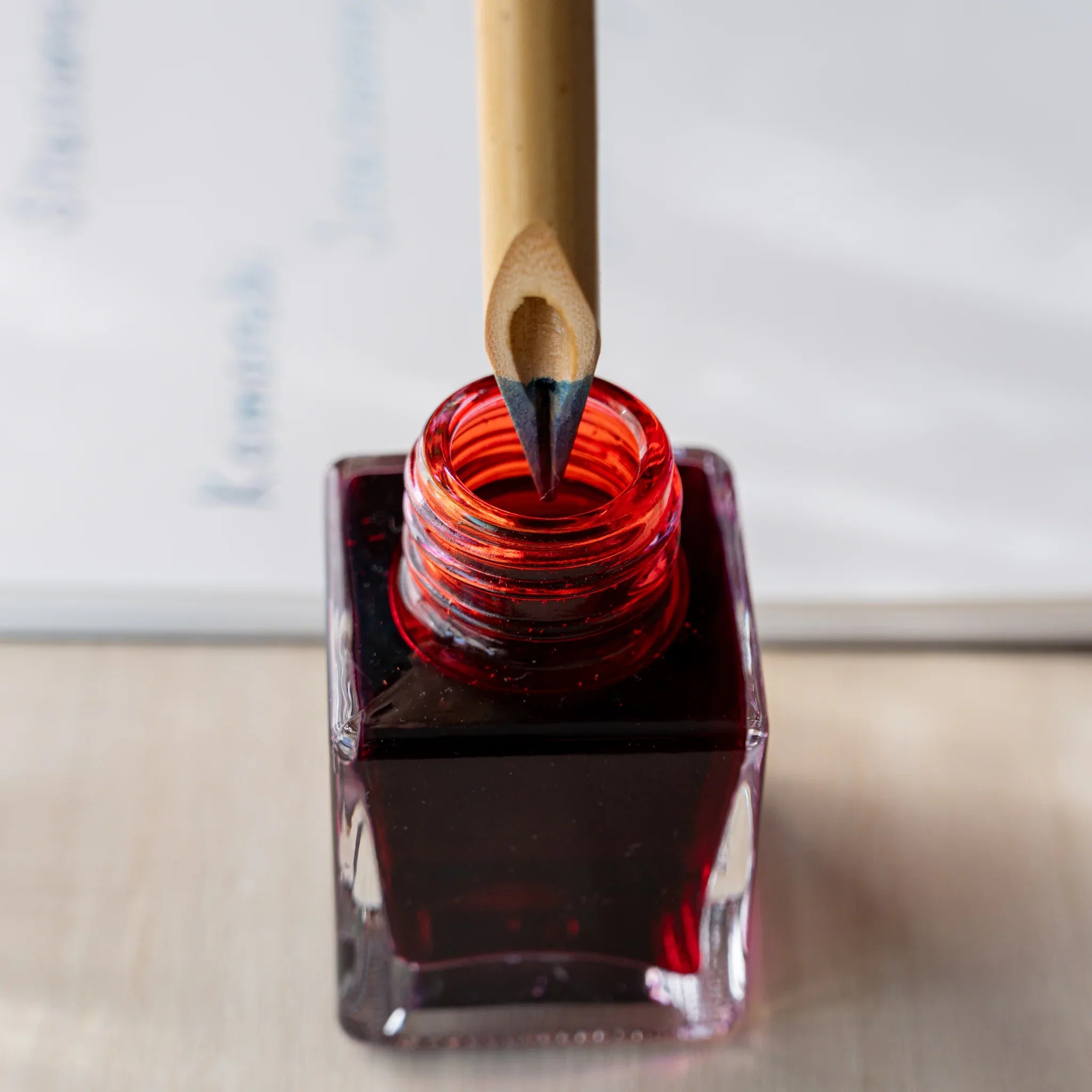 Boku-Undo bamboo dip pen nib dipping into an open square glass bottle filled with deep red ink