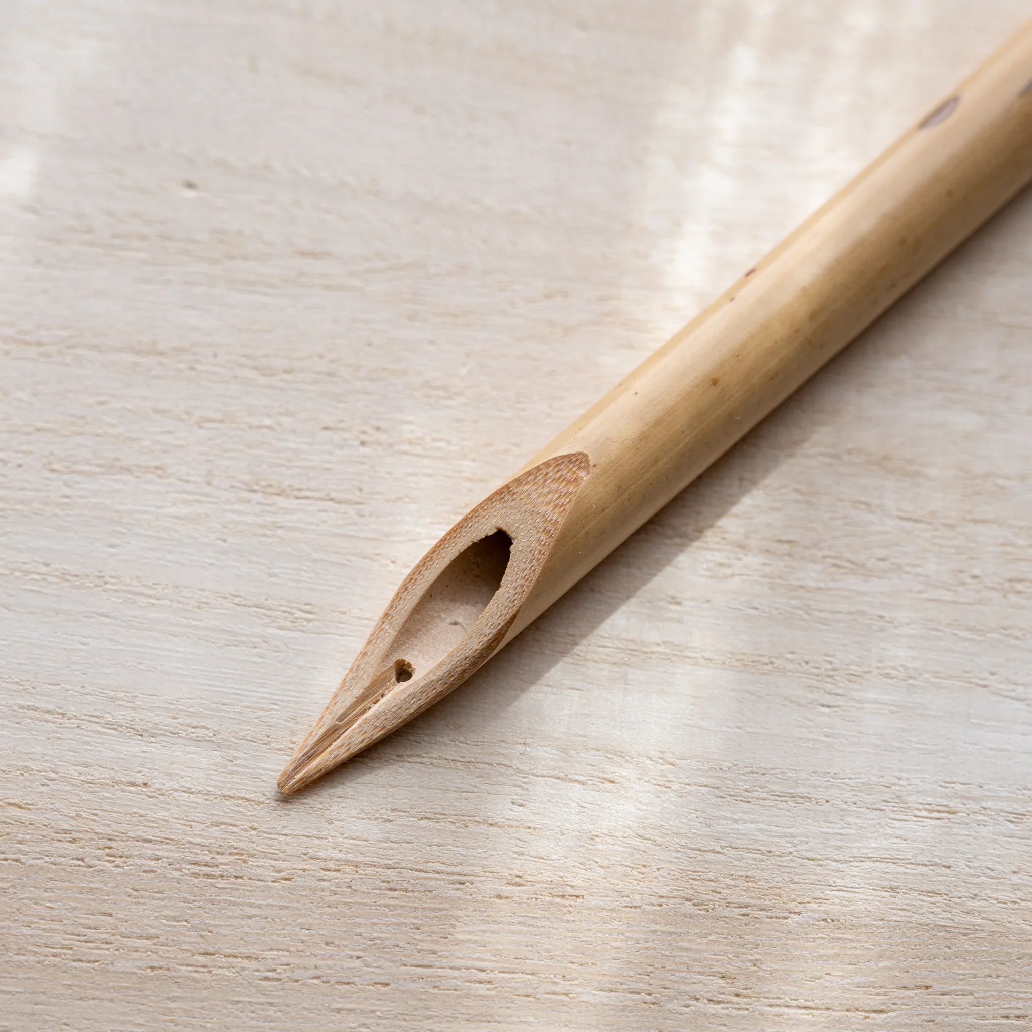 Close-up of Boku-Undo bamboo dip pen tip showing split hollow bamboo nib with natural wood grain on wooden surface