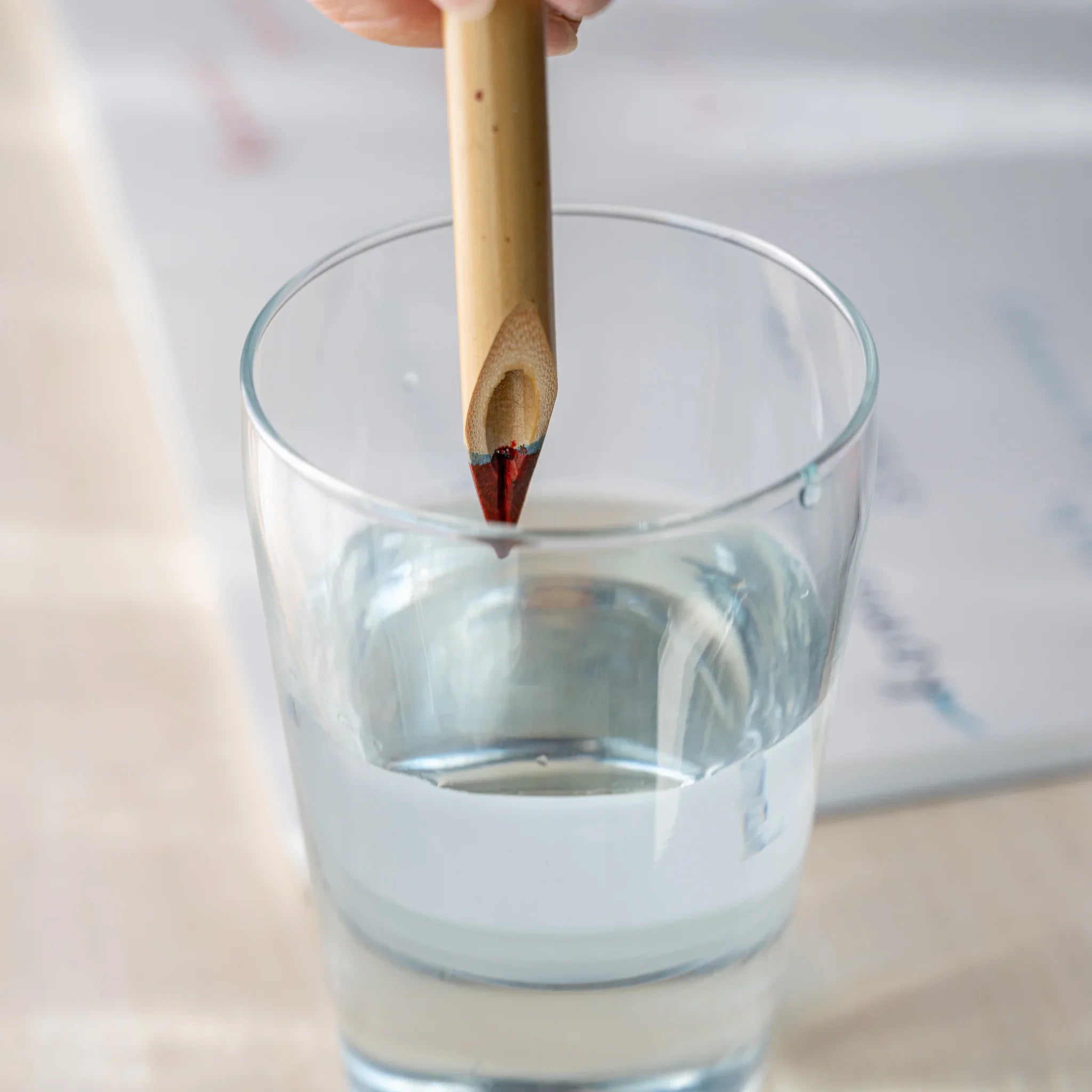 Hand rinsing Boku-Undo bamboo dip pen with red ink on nib in a clear glass of water