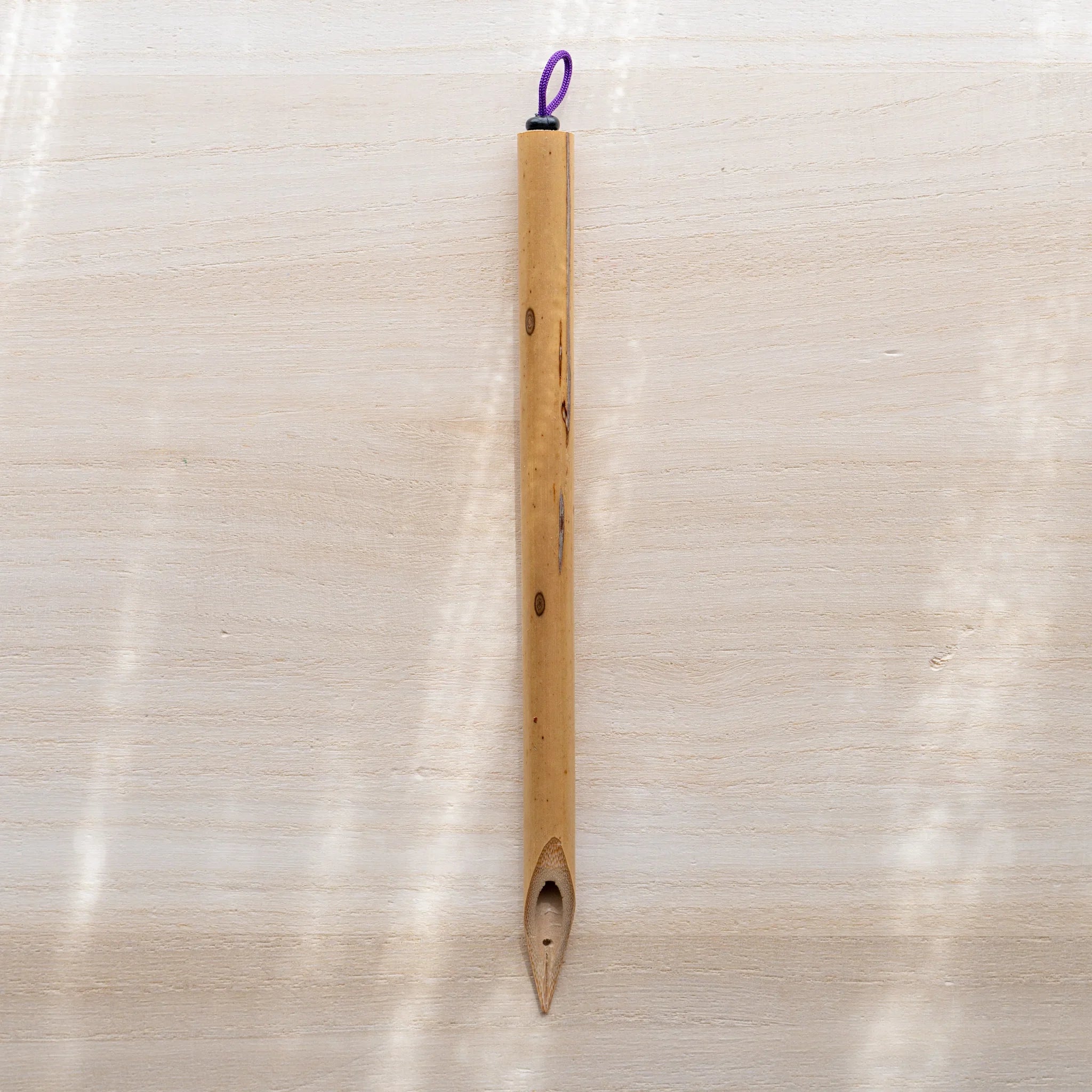 Boku-Undo bamboo dip pen laid flat on light wooden surface, showing full length with purple hanging loop at top