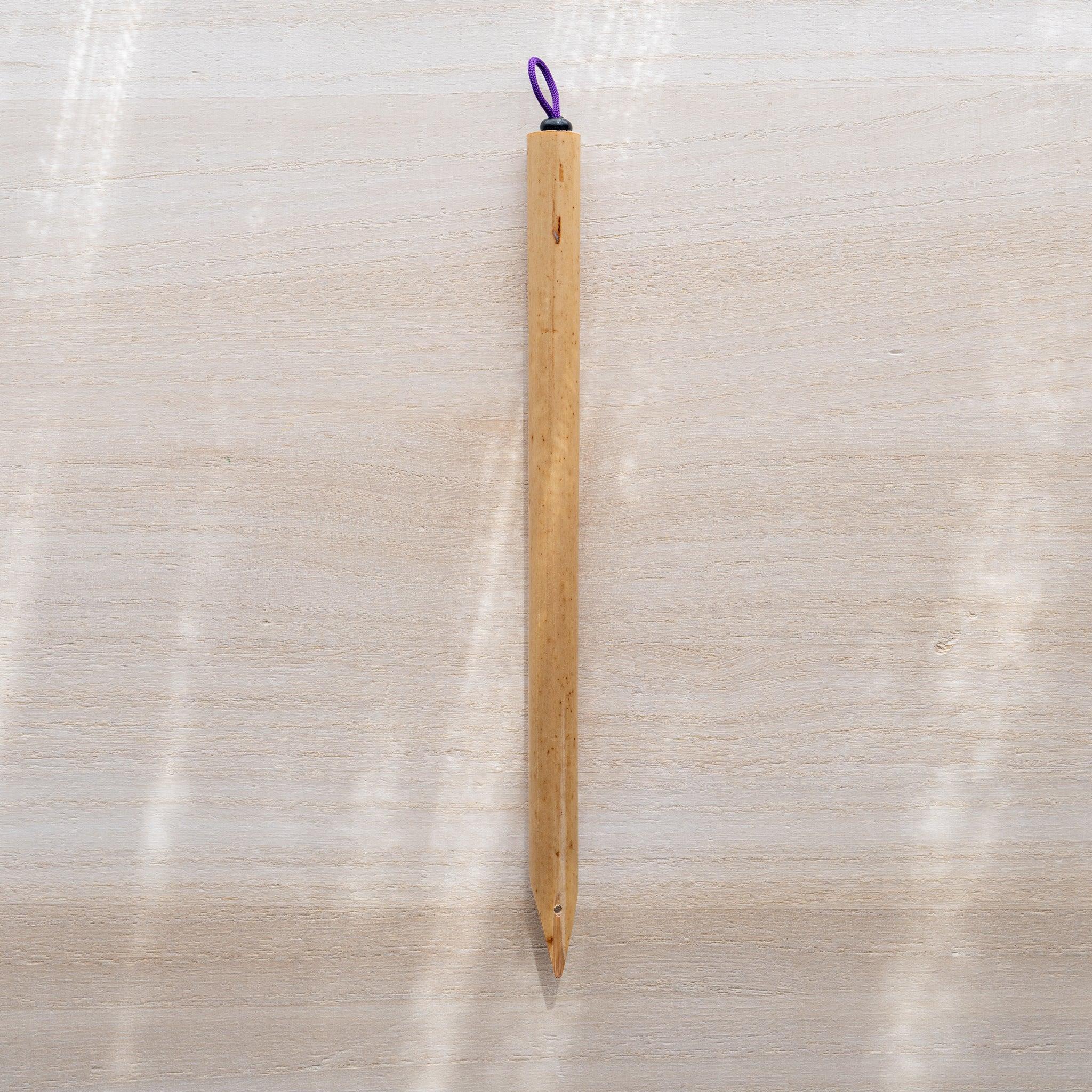 Boku-Undo bamboo dip pen standing upright on light wooden surface, purple loop at top and pointed nib at bottom