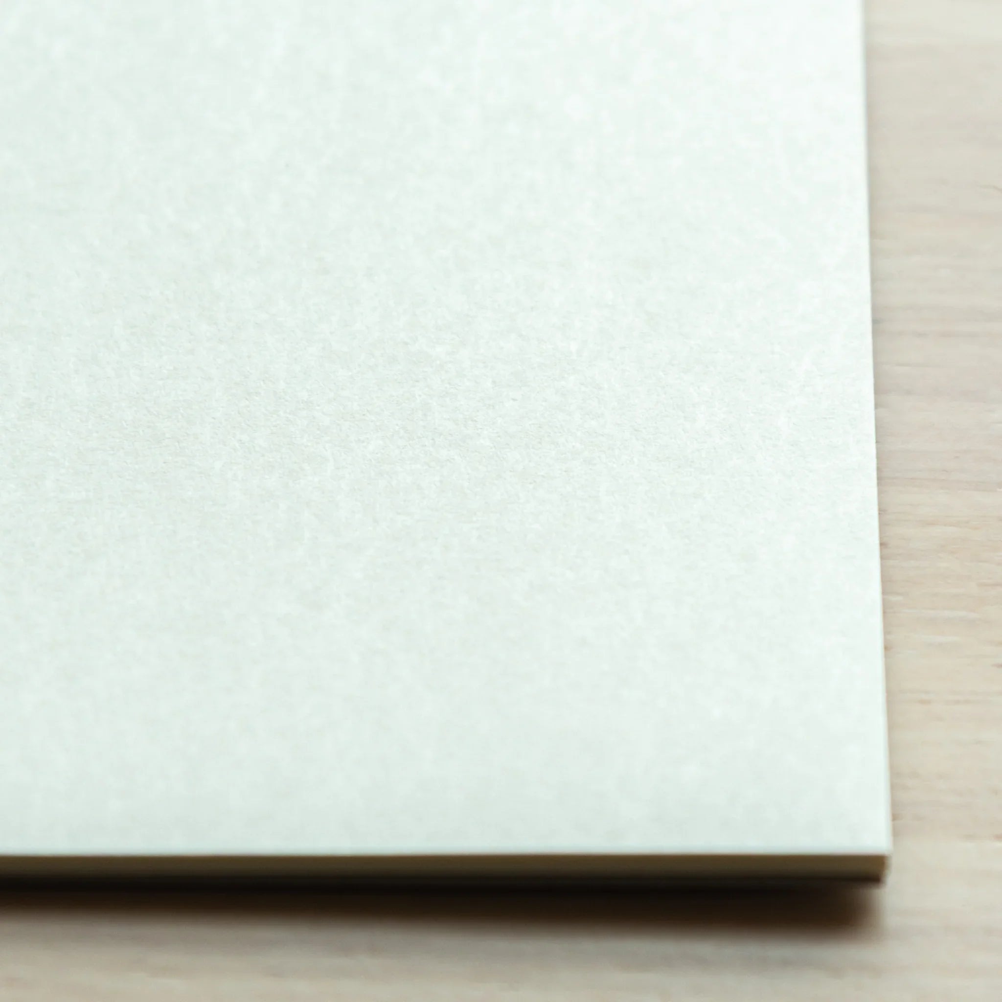 Close-up corner of Soliste writing pad on light wood, bright white paper surface and stacked sheet edges visible