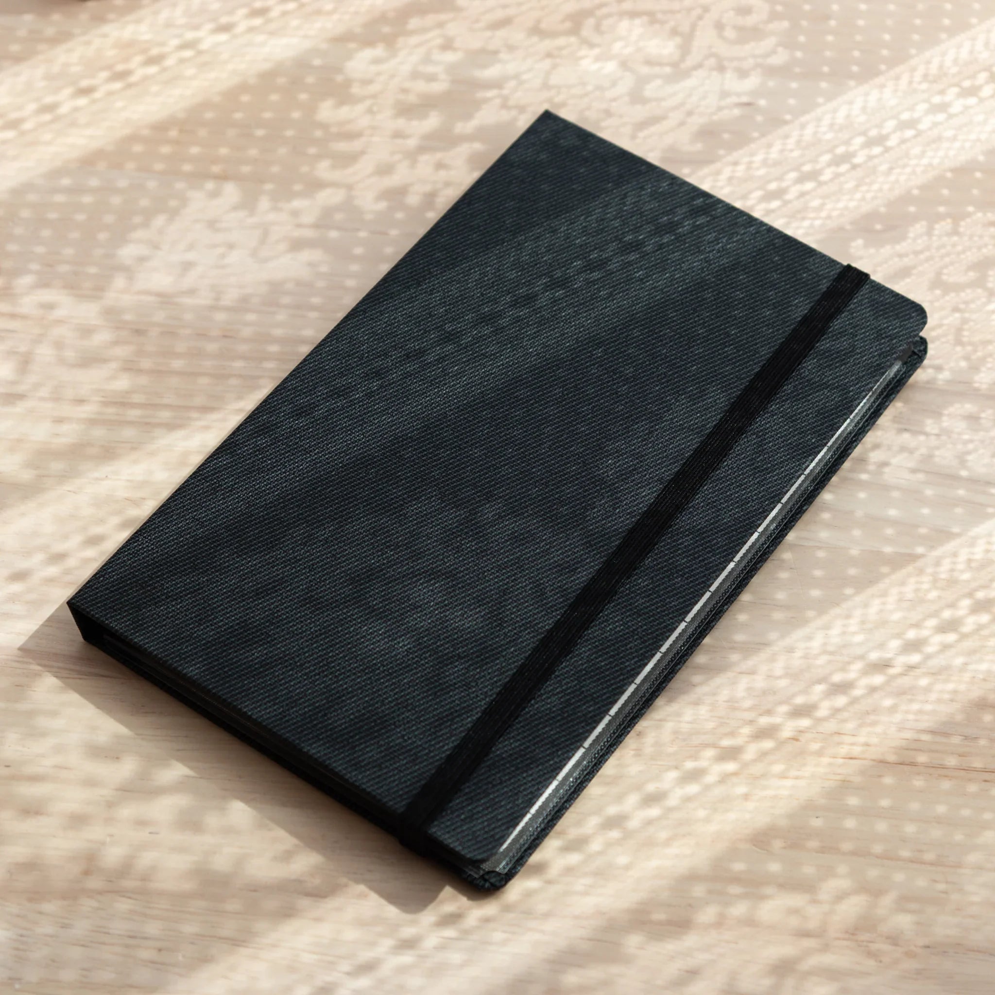 Side view of closed Bullet Jotter black gabardine cover on textured surface, stacked writing pad pages visible at right