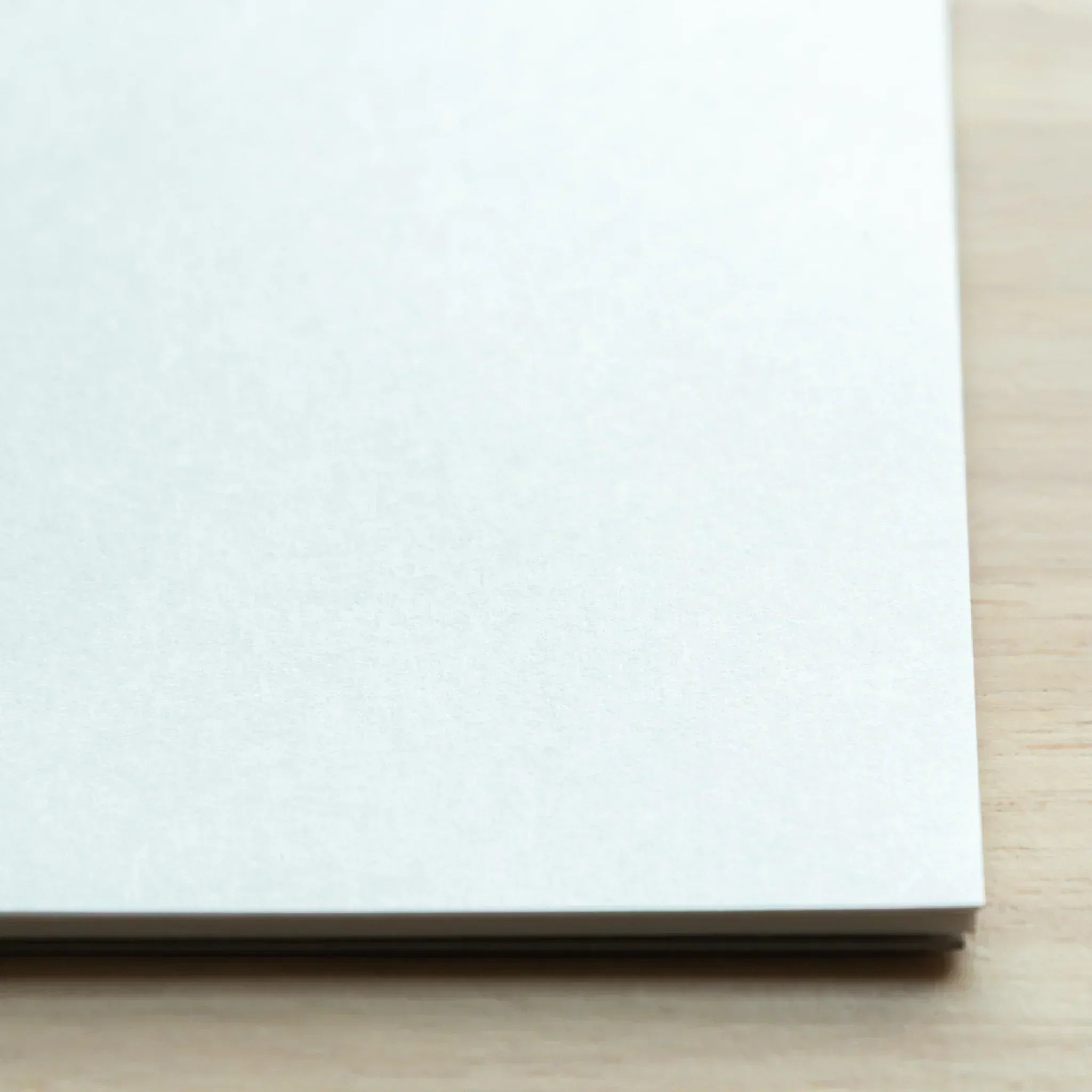 Close-up corner view of Bullet Jotter writing pad on light wood, showing white paper pages and stacked sheet edges