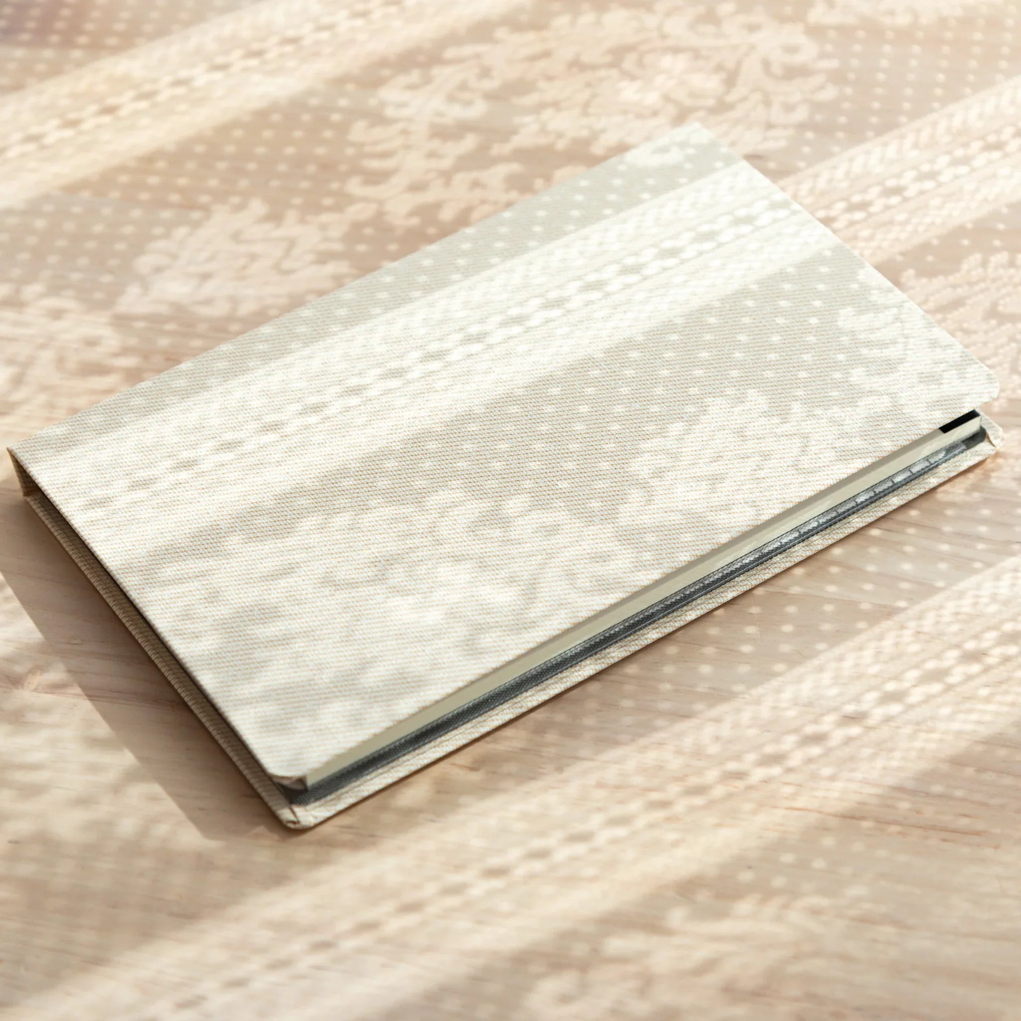 Side view of closed Bullet Jotter ivory white gabardine cover, stacked writing pad pages visible between front and back
