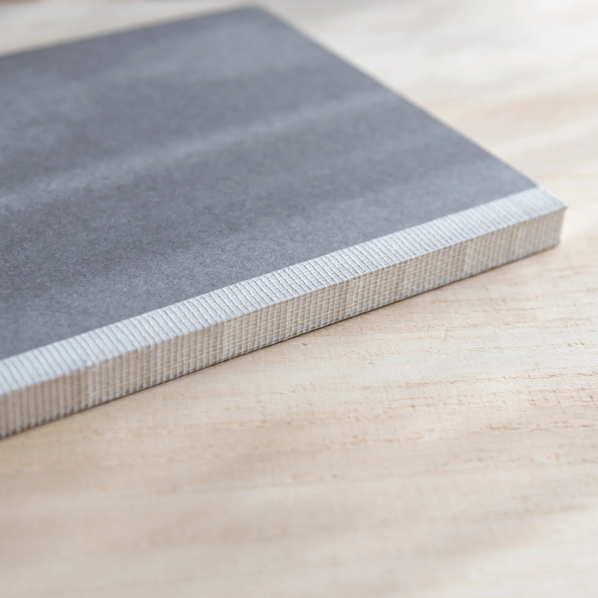 Close-up side view of a Japanese Notebook showing its thick page edges on a wooden table.