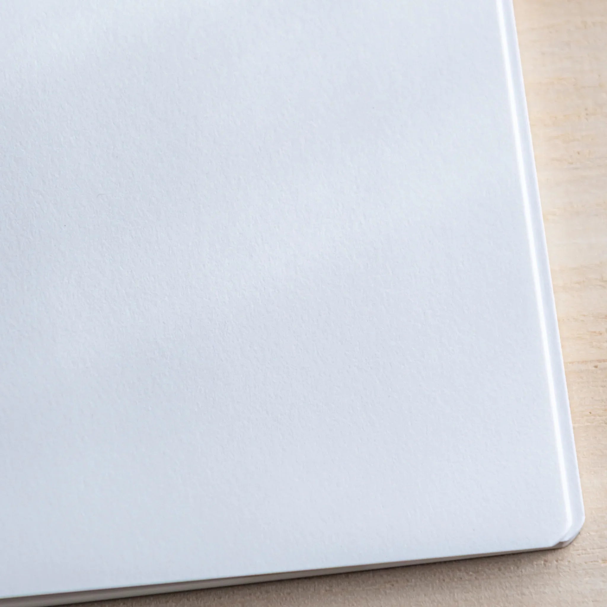 Close-up of Japanese Notebook showing a blank white page with curved corner on light wooden desk.