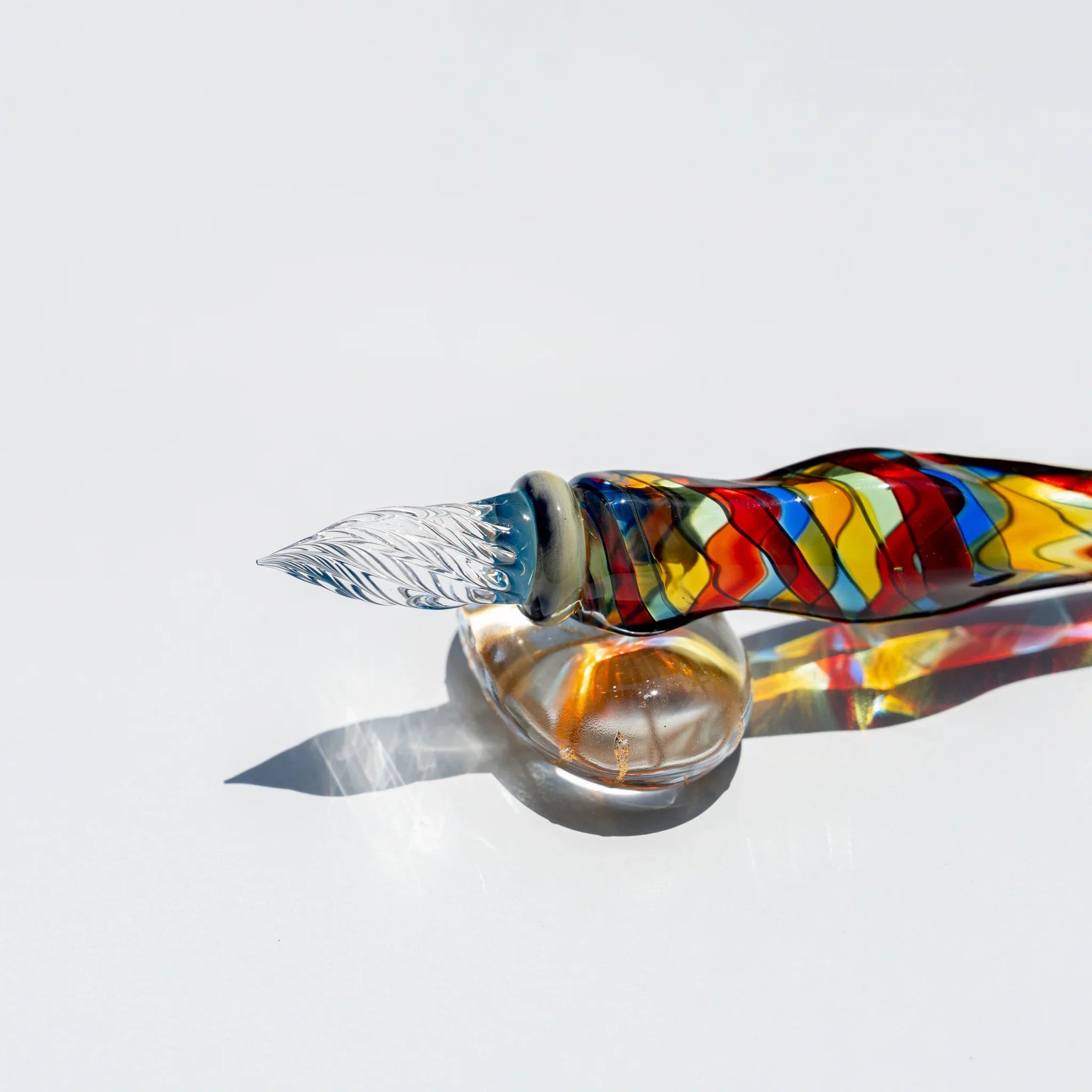 Side view of Cathedral glass dip pen on a glass ball rest, clear grooved nib, red, yellow, blue and green mosaic barrel