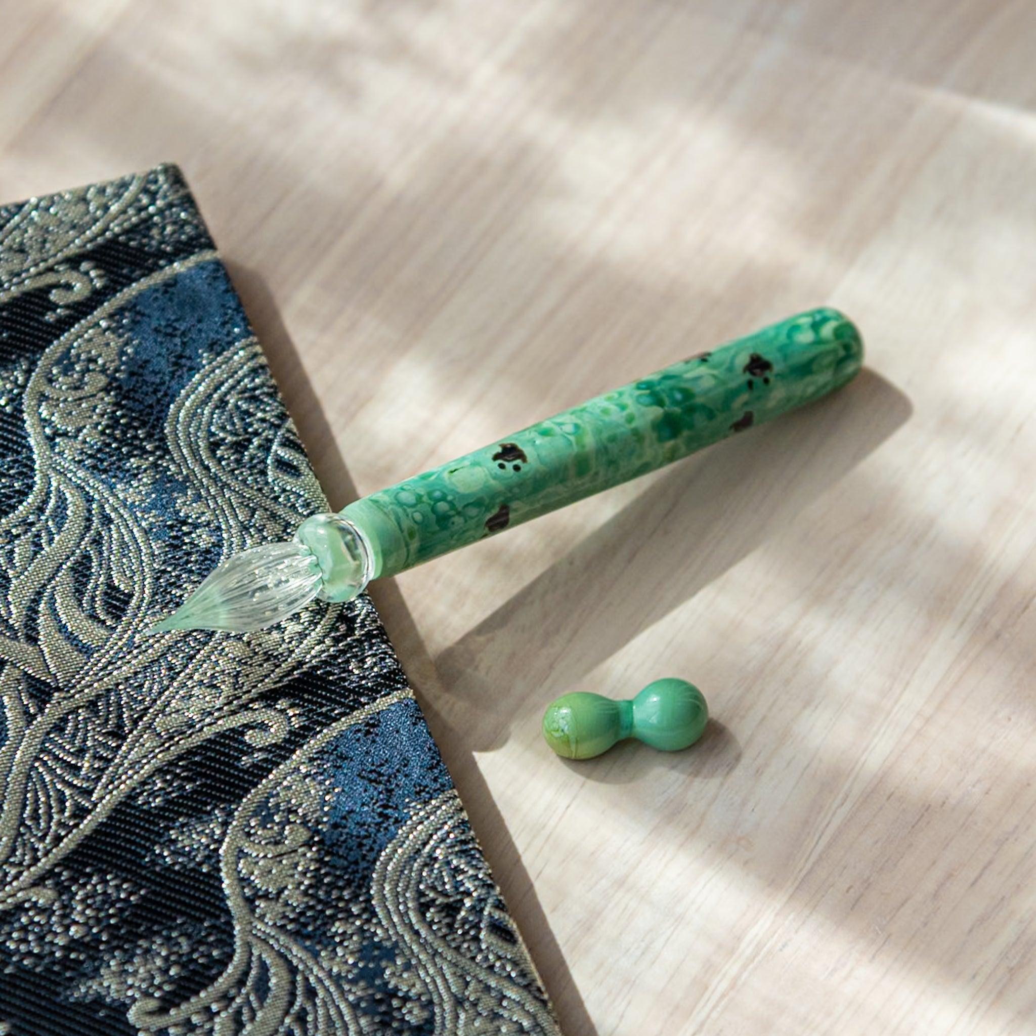 Emerald green glass pen with traditional Chidori design, showing birds over waves. Includes matching pen rest on wood and Nishijin textile notebook.