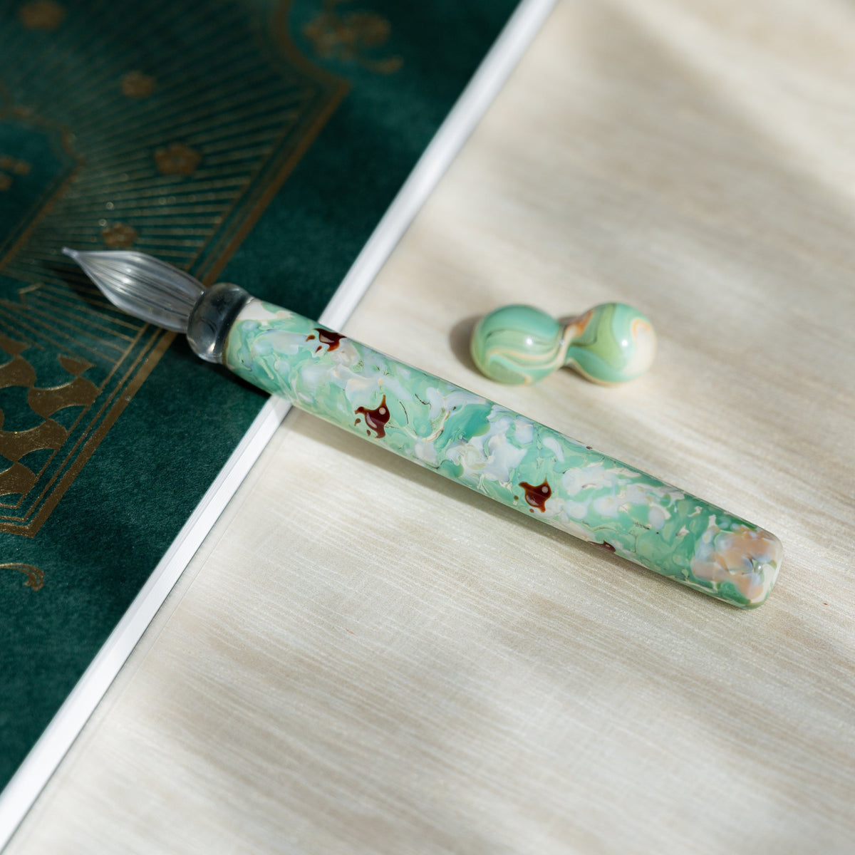 Chidori Mint Marble glass dip pen on a white page with its two-sphere green glass pen rest alongside