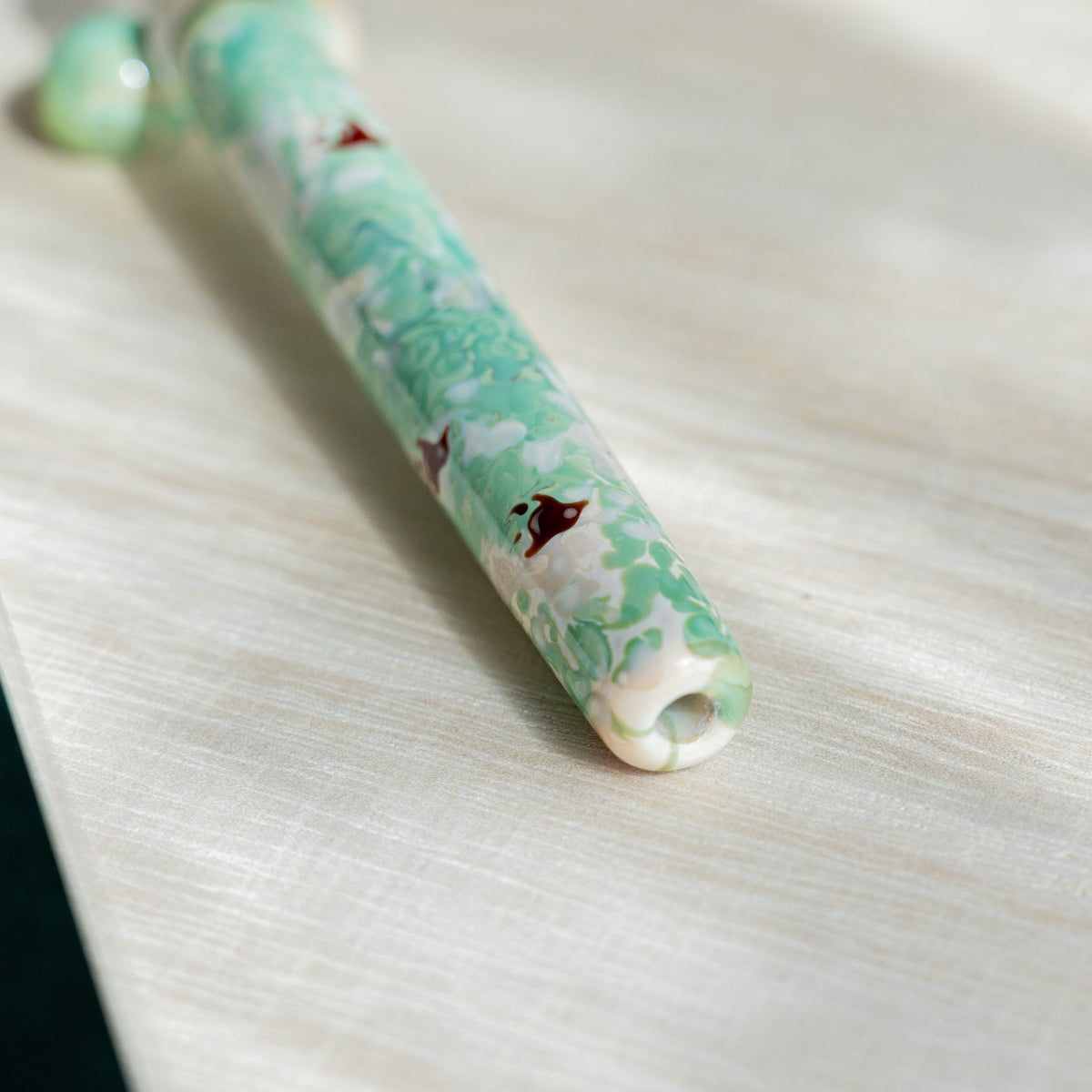 Detail of mint green and white marbled glass with a dark red plover motif along the pen barrel
